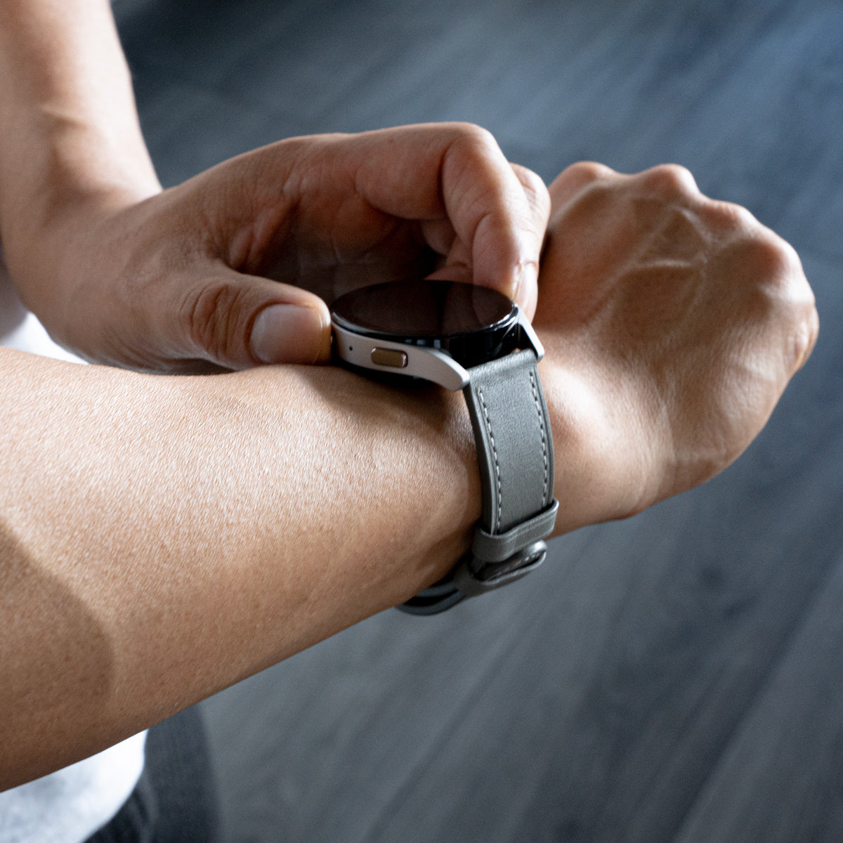 Eine Person justiert mit der Hand eine Smartwatch an ihrem Handgelenk. Die Uhr hat ein graues Armband und einen schwarzen Bildschirm.