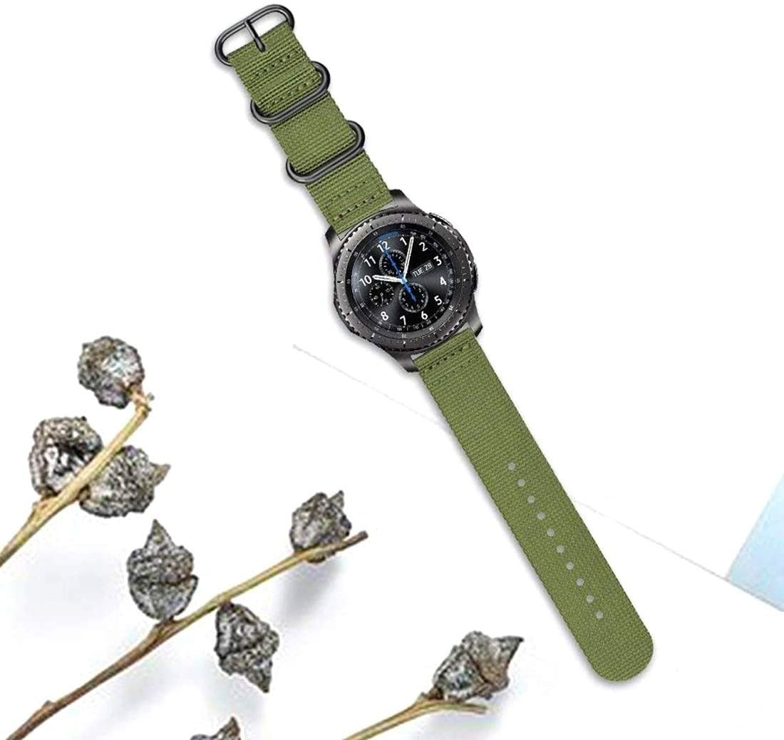 Eine schwarze Smartwatch mit olivgrünem Armband liegt diagonal. Getrocknete Zweige mit kleinen Knospen sind in der linken unteren Ecke.