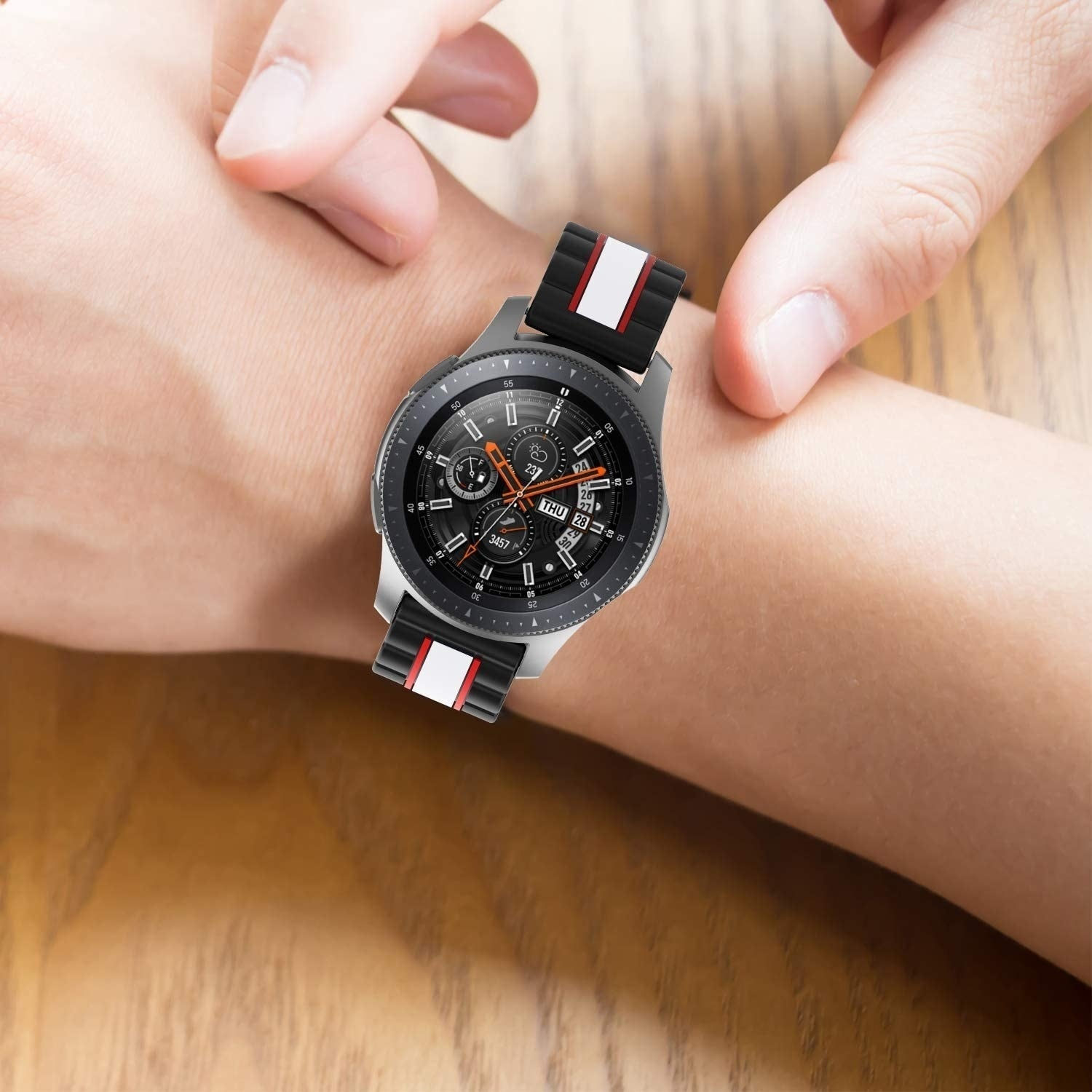 Eine Person trägt eine Smartwatch. Die Uhr hat ein schwarzes Zifferblatt und ein schwarzes Armband mit roten und weißen Details. Die Uhr ist am Handgelenk.
