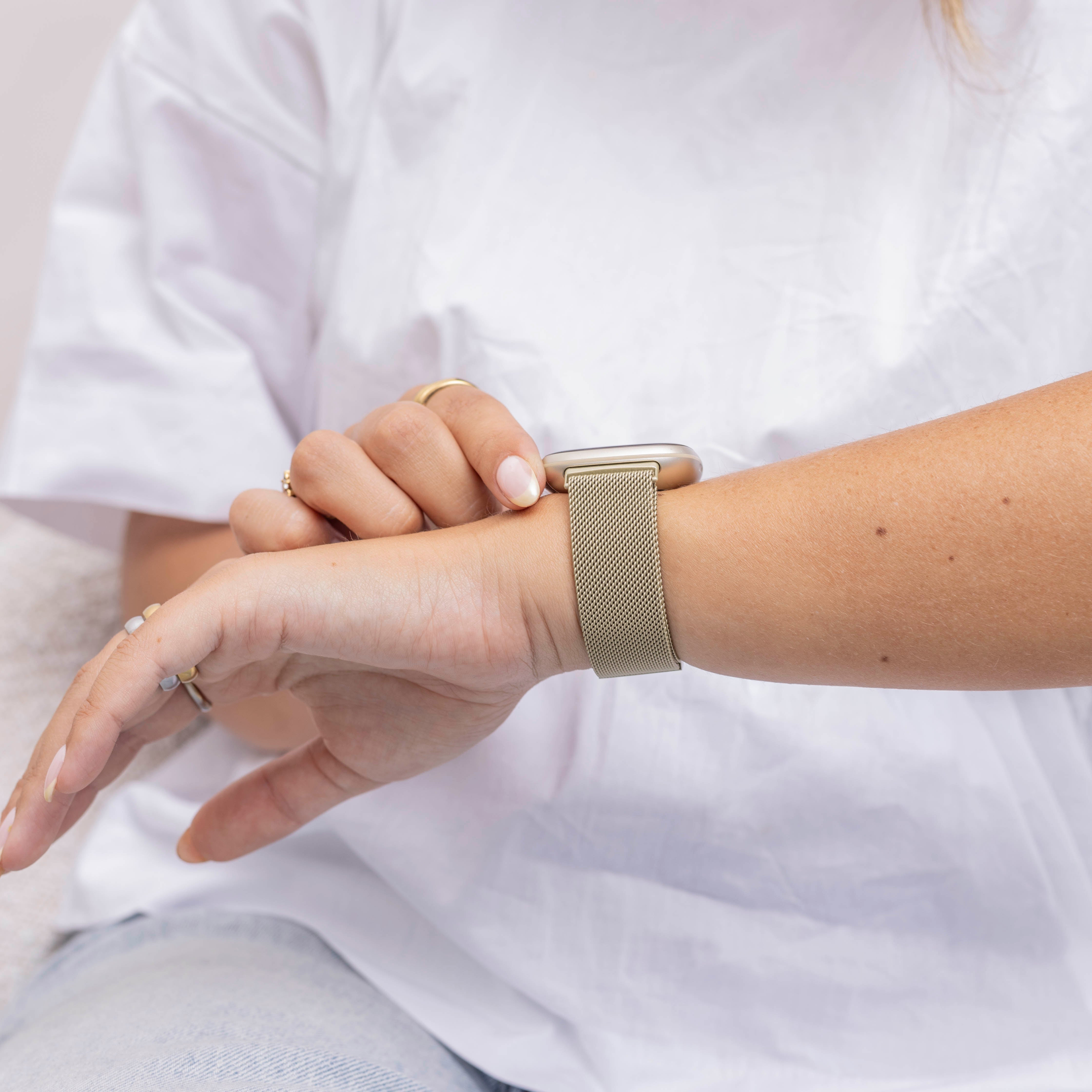 Eine Person mit weißem Hemd und grüner Armbanduhr betrachtet ihre Uhr am Handgelenk.