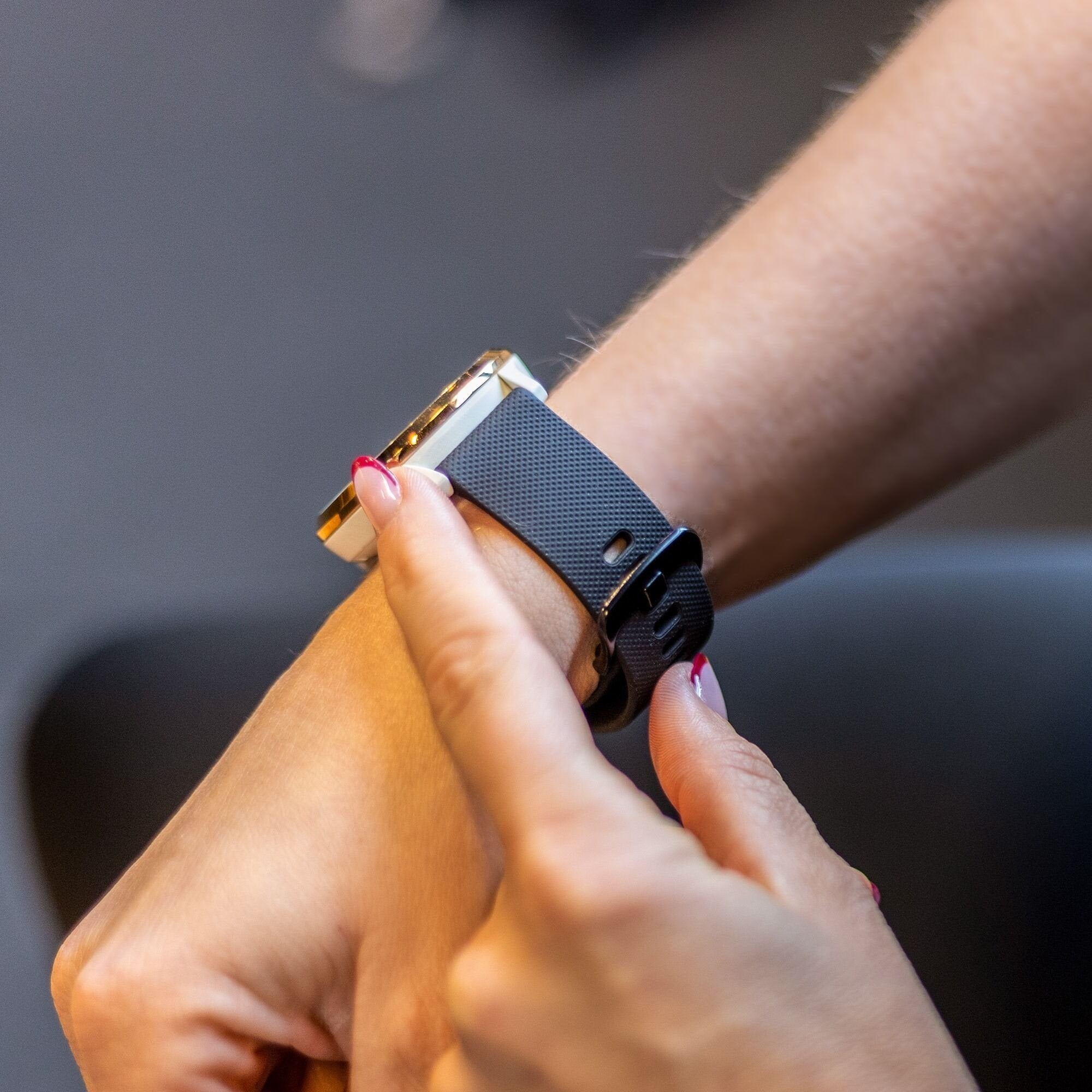 Handgelenk mit Smartwatch, schwarzem Armband und goldenen Akzenten. Finger mit roten Nägeln justieren die Uhr.