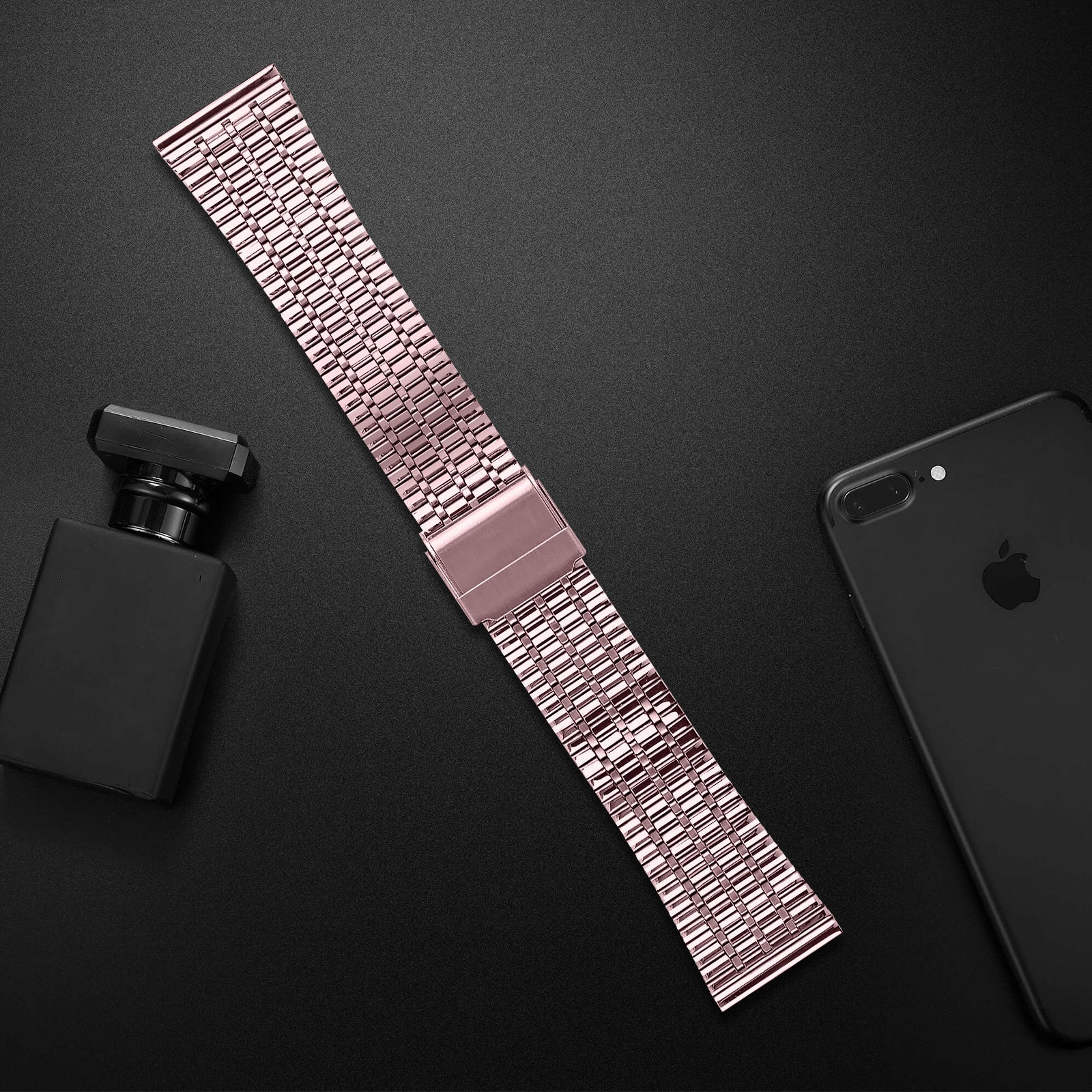 Roségoldenes Armband, schwarzes Telefon und Parfümflasche auf schwarzer Oberfläche.