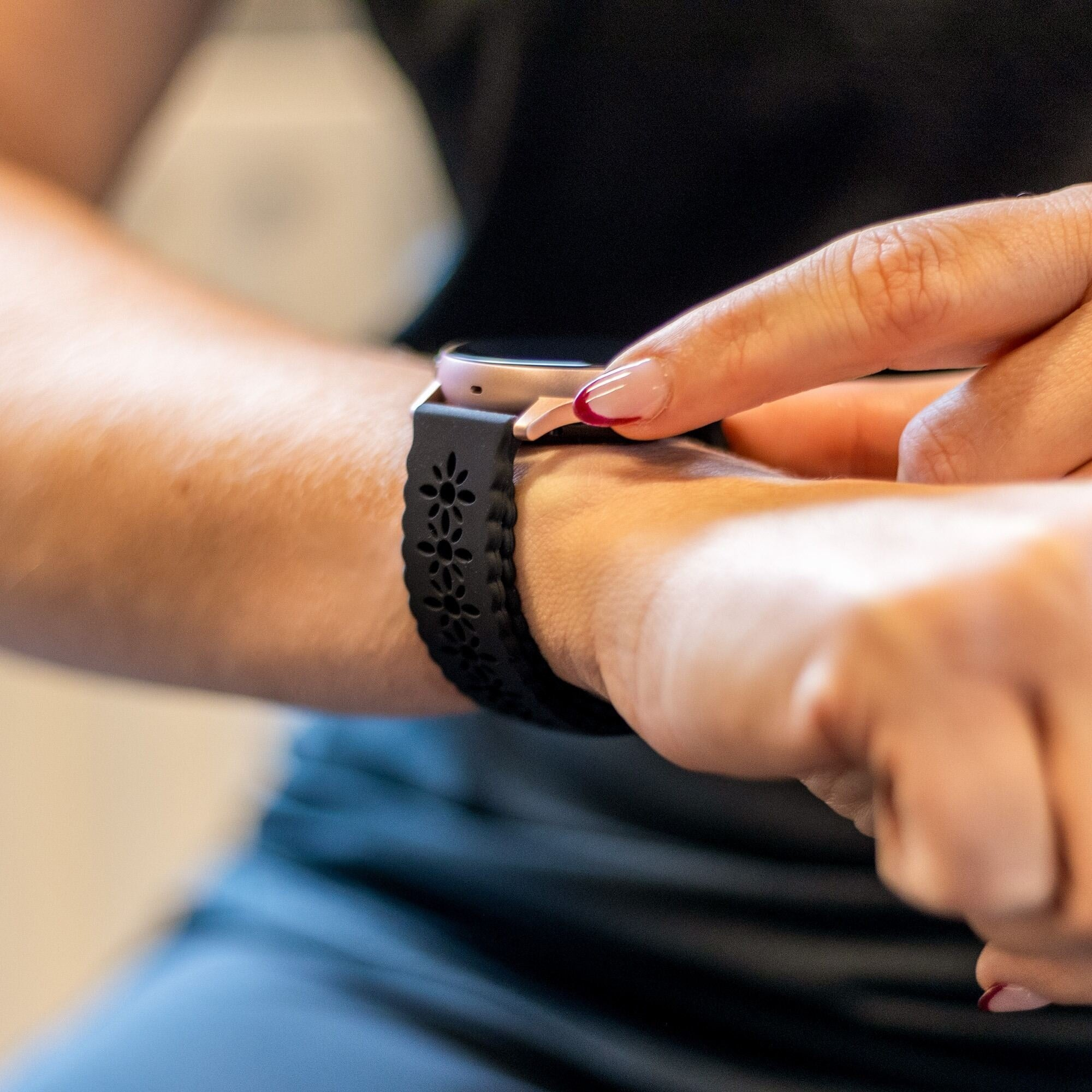 Die Hand einer Frau berührt eine Smartwatch mit einem schwarzen Blumenarmband. Die Nägel sind rot lackiert.