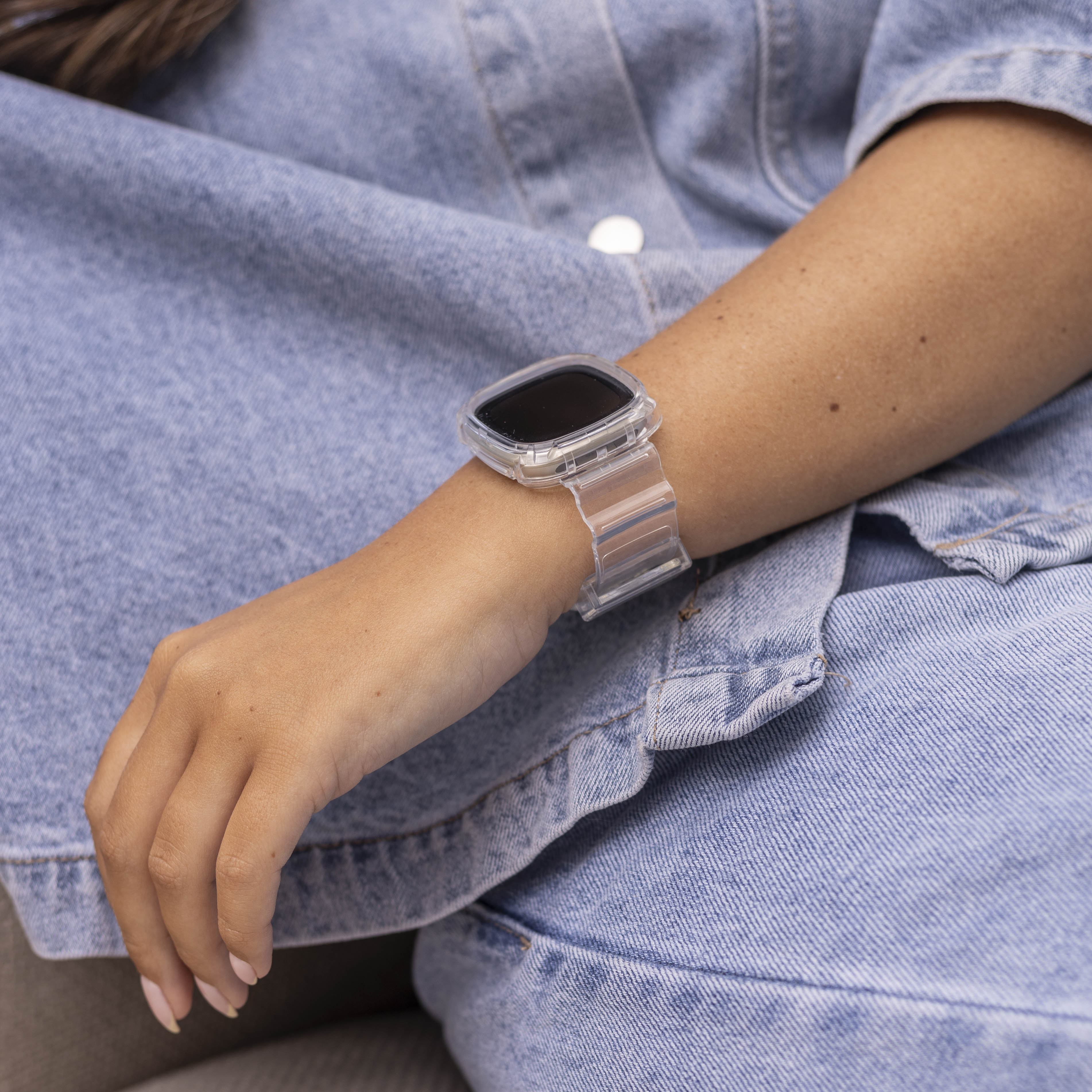 Ein Arm mit einer transparenten Uhr mit schwarzem Bildschirm. Die Person trägt eine Jeansjacke.