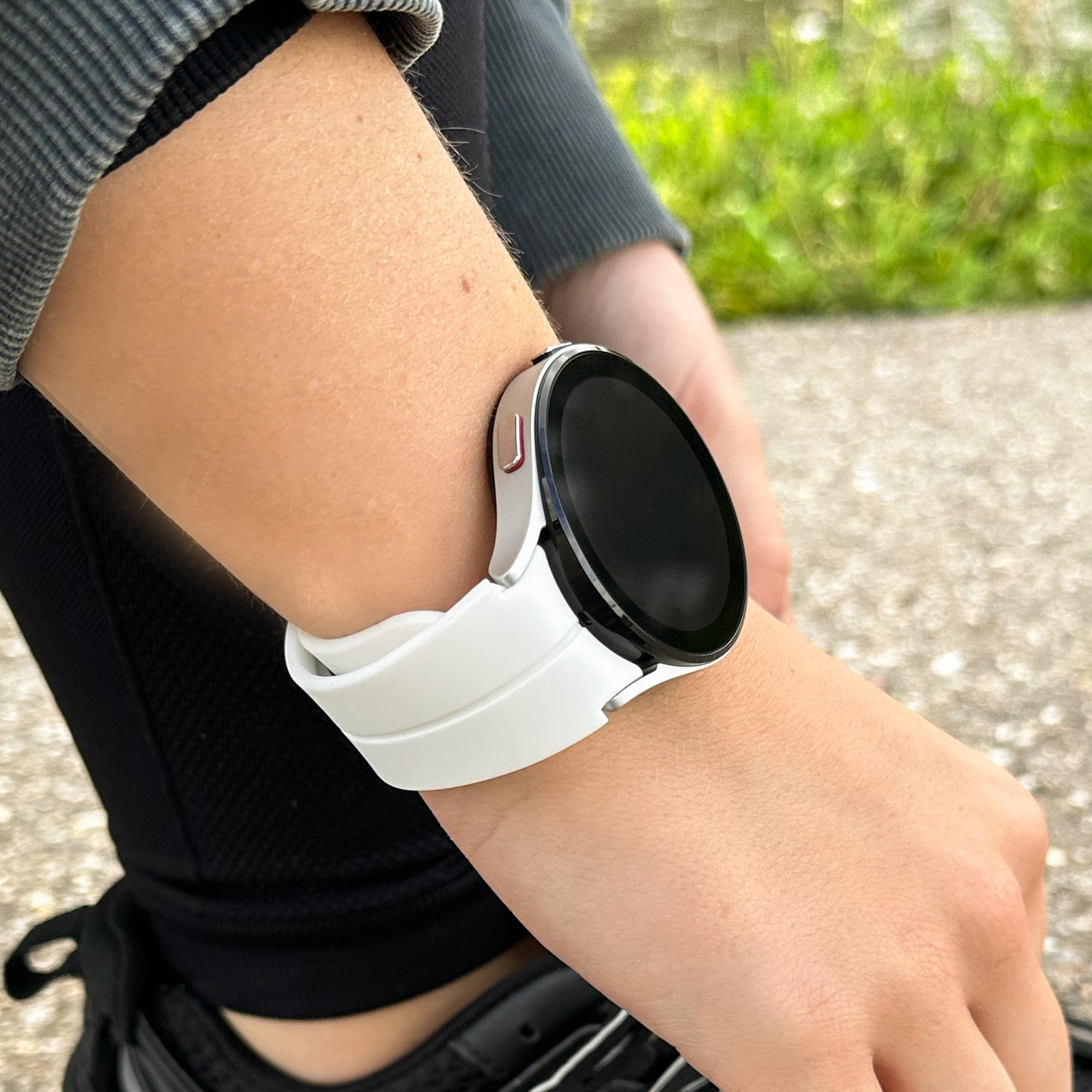 Eine Person trägt eine weiße Smartwatch. Die Uhr zeigt einen schwarzen Bildschirm und befindet sich an einem hellhäutigen Handgelenk. Hintergrund ist verschwommen.