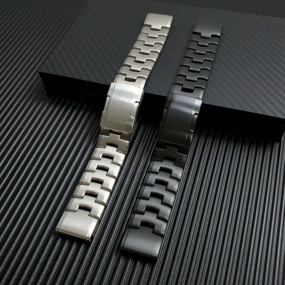 Zwei Uhrenarmbänder, eines silberfarben und eines schwarz, liegen auf einer strukturierten Oberfläche. Das silberne Band ist links.