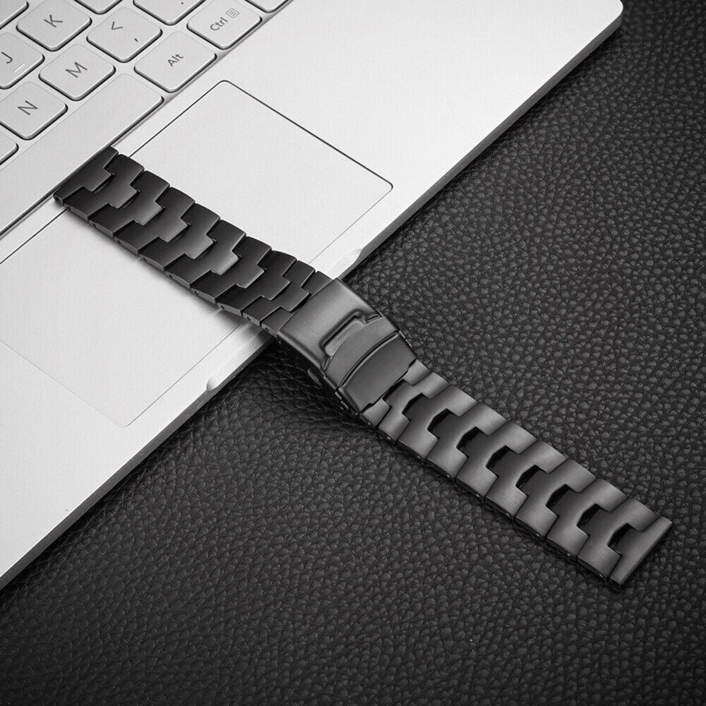 Ein schwarzes Uhrenarmband liegt auf einem Laptop und einer strukturierten schwarzen Oberfläche. Das Armband ist metallisch und hat einen Verschluss.