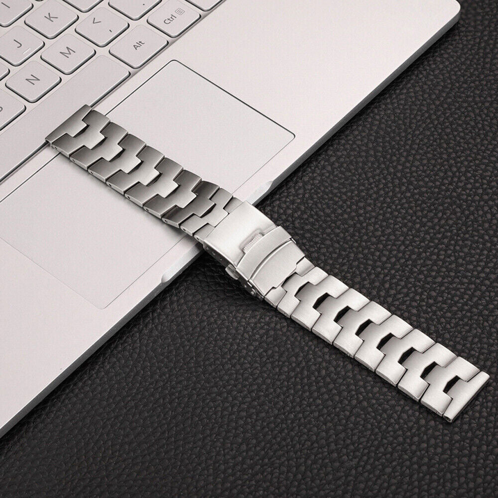 Silbernes Uhrenarmband auf einem Laptop und einer schwarzen Lederoberfläche. Das Armband ist metallisch und hat einen Verschluss.