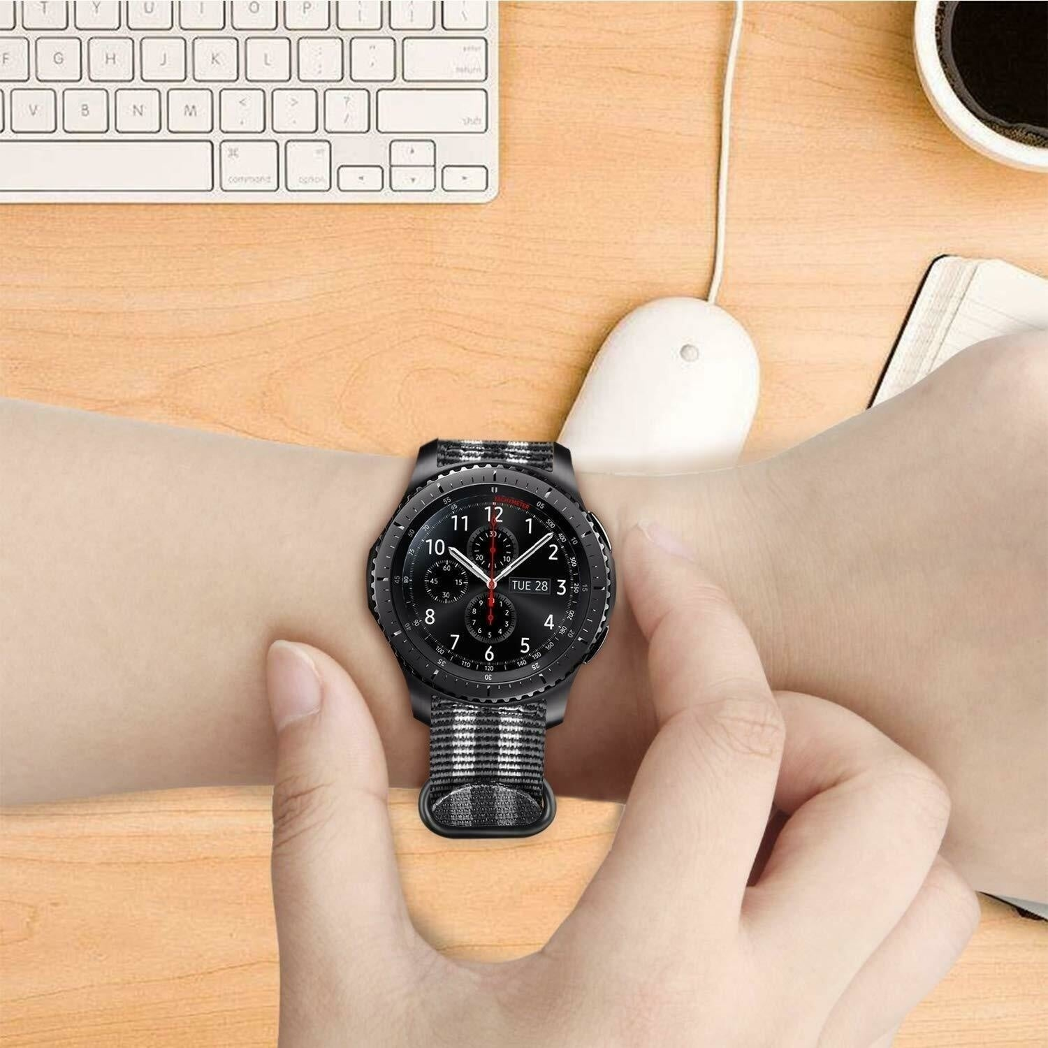 Ein Handgelenk mit einer schwarzen Uhr, die die Zeit anzeigt, wird von Händen gehalten. Eine Tastatur, Maus und ein Notizbuch sind sichtbar.