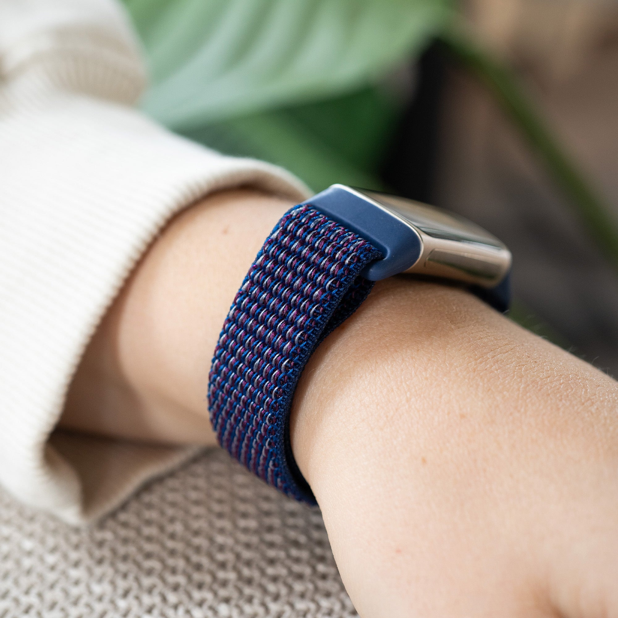 Handgelenk mit blau-lila gewebtem Armband. Die Uhr hat ein silbernes Zifferblatt und befindet sich am Handgelenk der Person.
