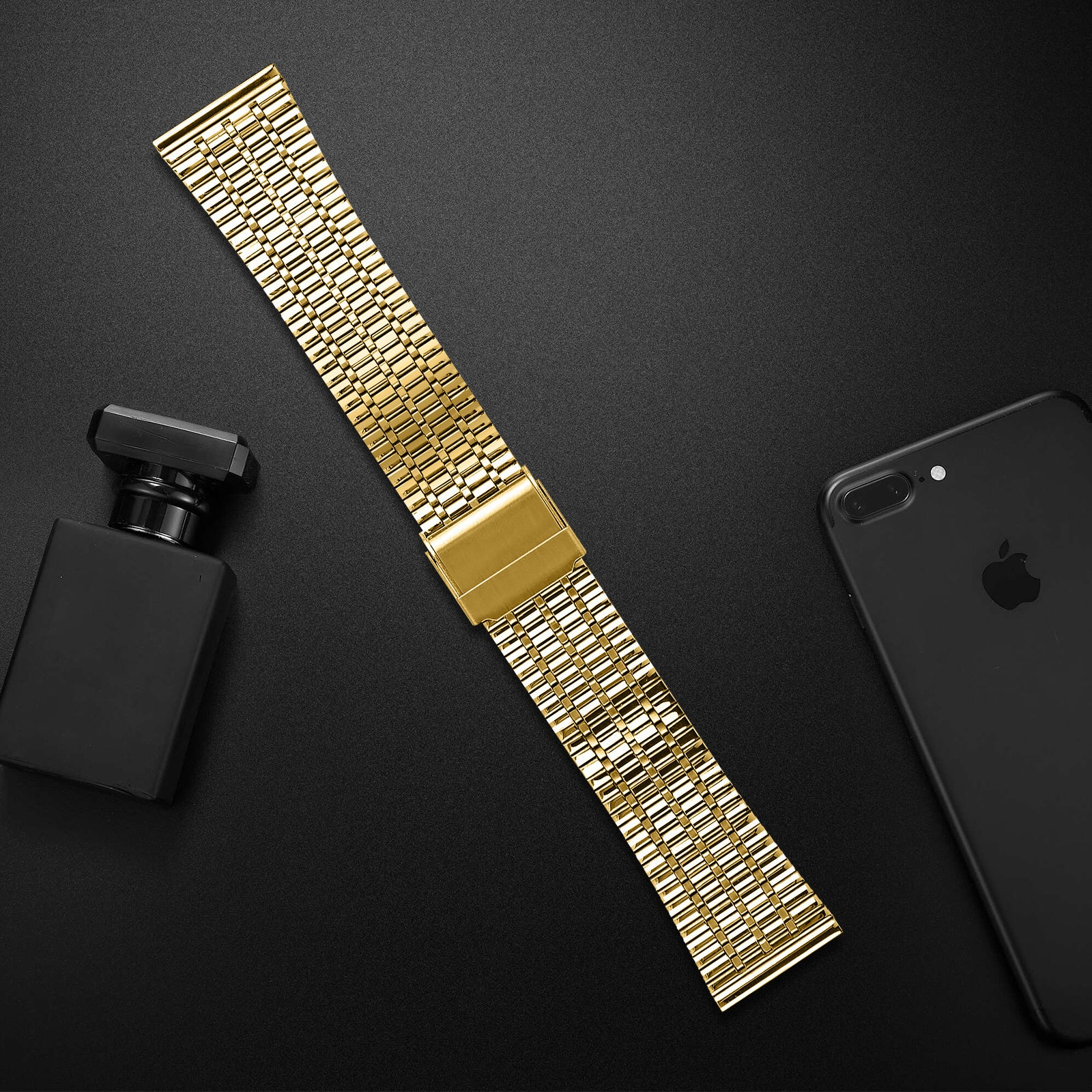 Ein goldenes Uhrenarmband, eine schwarze Parfümflasche und ein schwarzes Telefon auf schwarzem Untergrund.