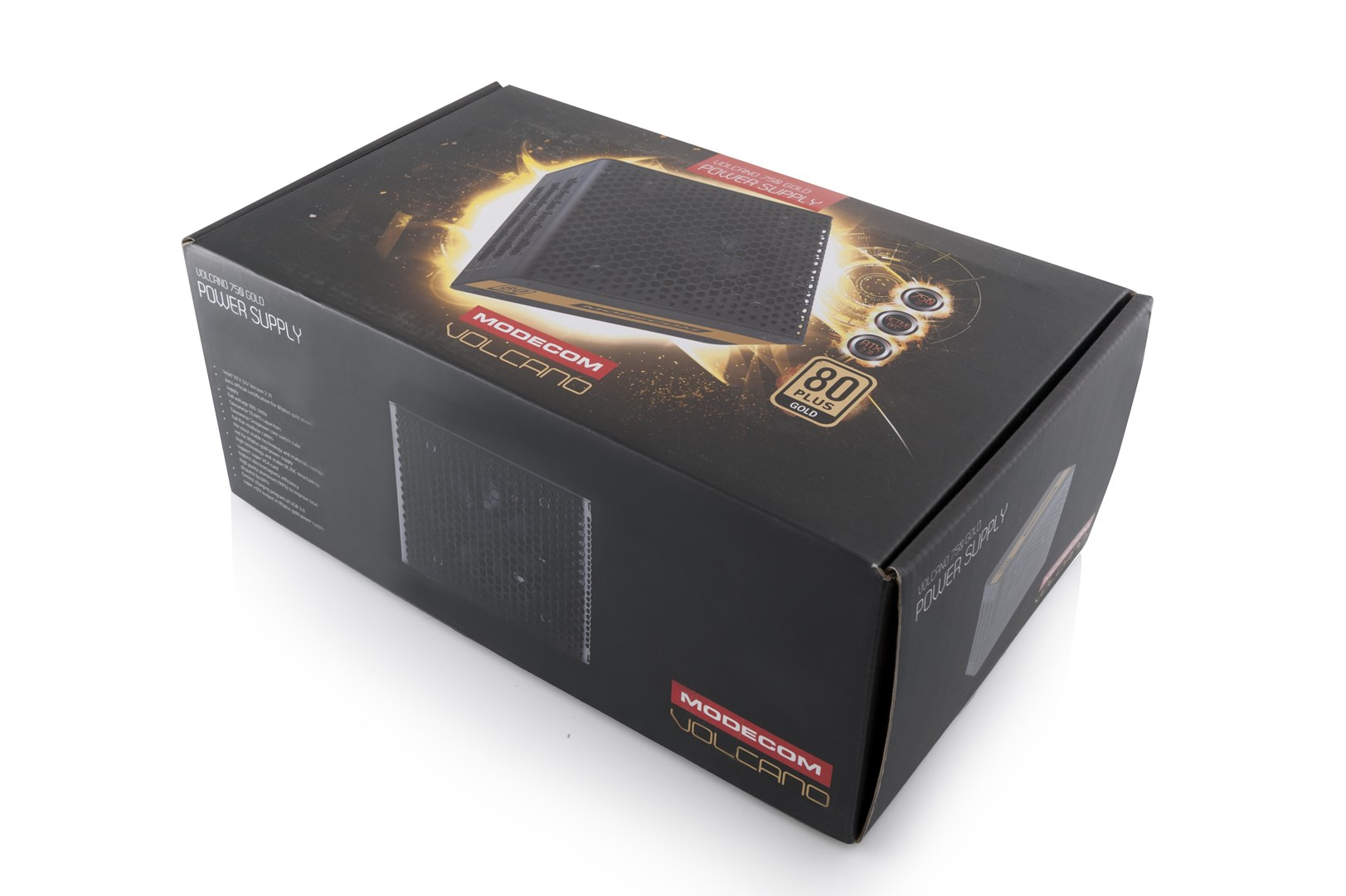 Una scatola di alimentatore Modecom Volcano 750 Gold. È nera con dettagli dorati. La scatola è angolata su una superficie bianca.