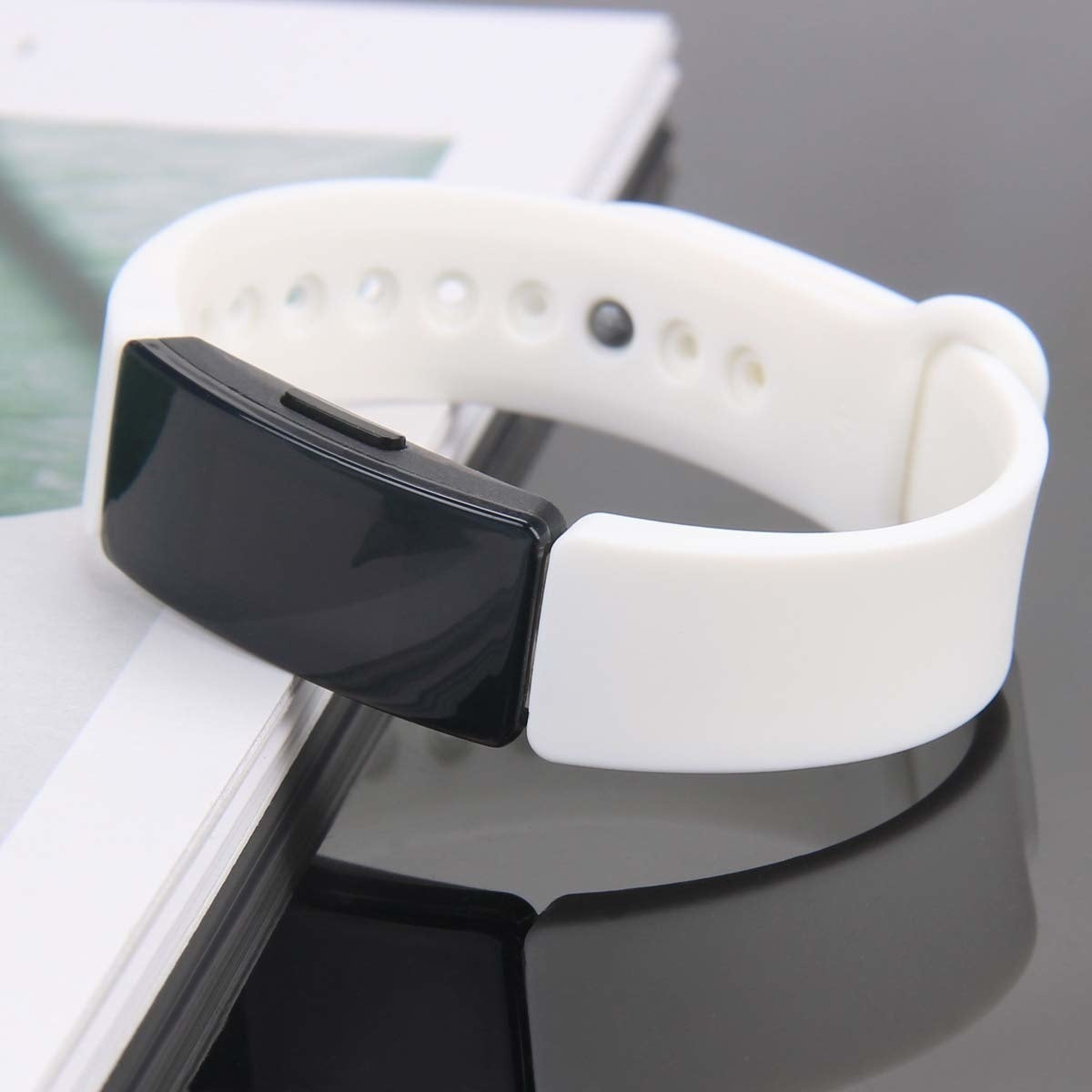 Ein weißes und schwarzes Fitness-Tracker-Armband liegt auf einer reflektierenden Oberfläche, vermutlich einem Tisch. Das Band ist weiß, mit schwarzem Display.