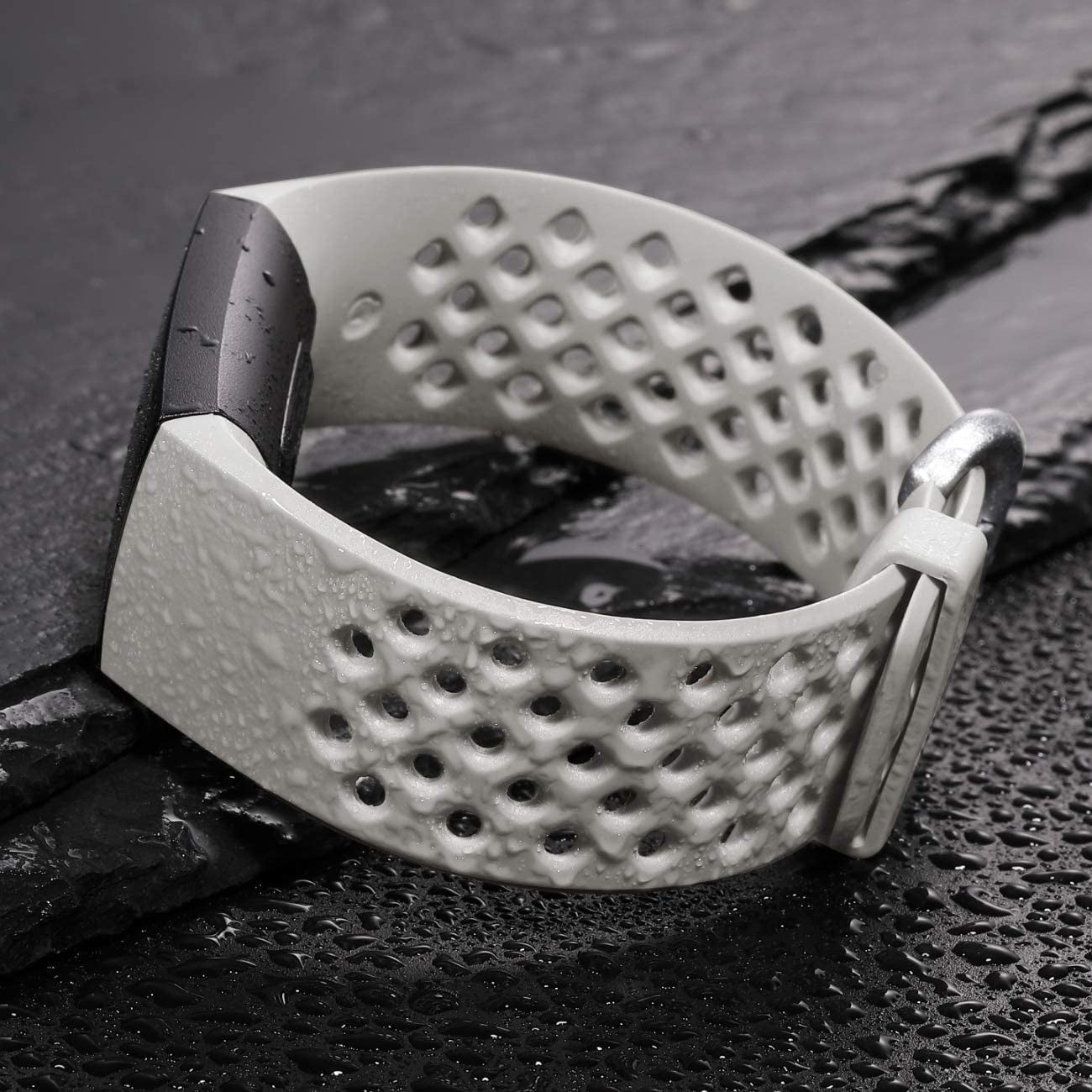 Ein weißes Smartwatch-Armband mit Löchern, einem dunkelgrauen Verschluss und einer silbernen Schnalle auf einer nassen, schwarzen Oberfläche.
