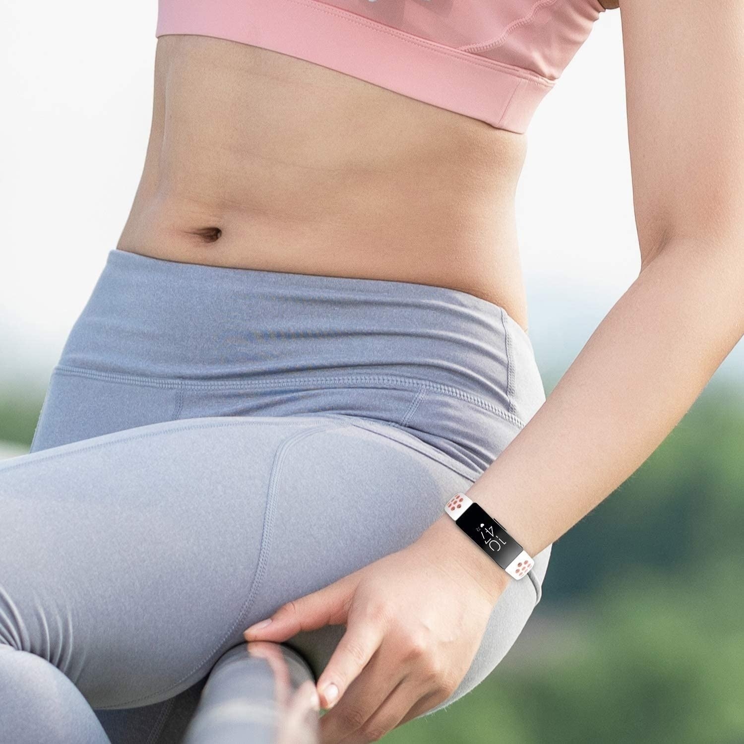Frau in Sportkleidung mit Fitness-Tracker am Handgelenk. Sie hält eine Metallstange. Der Hintergrund ist verschwommen und grün.