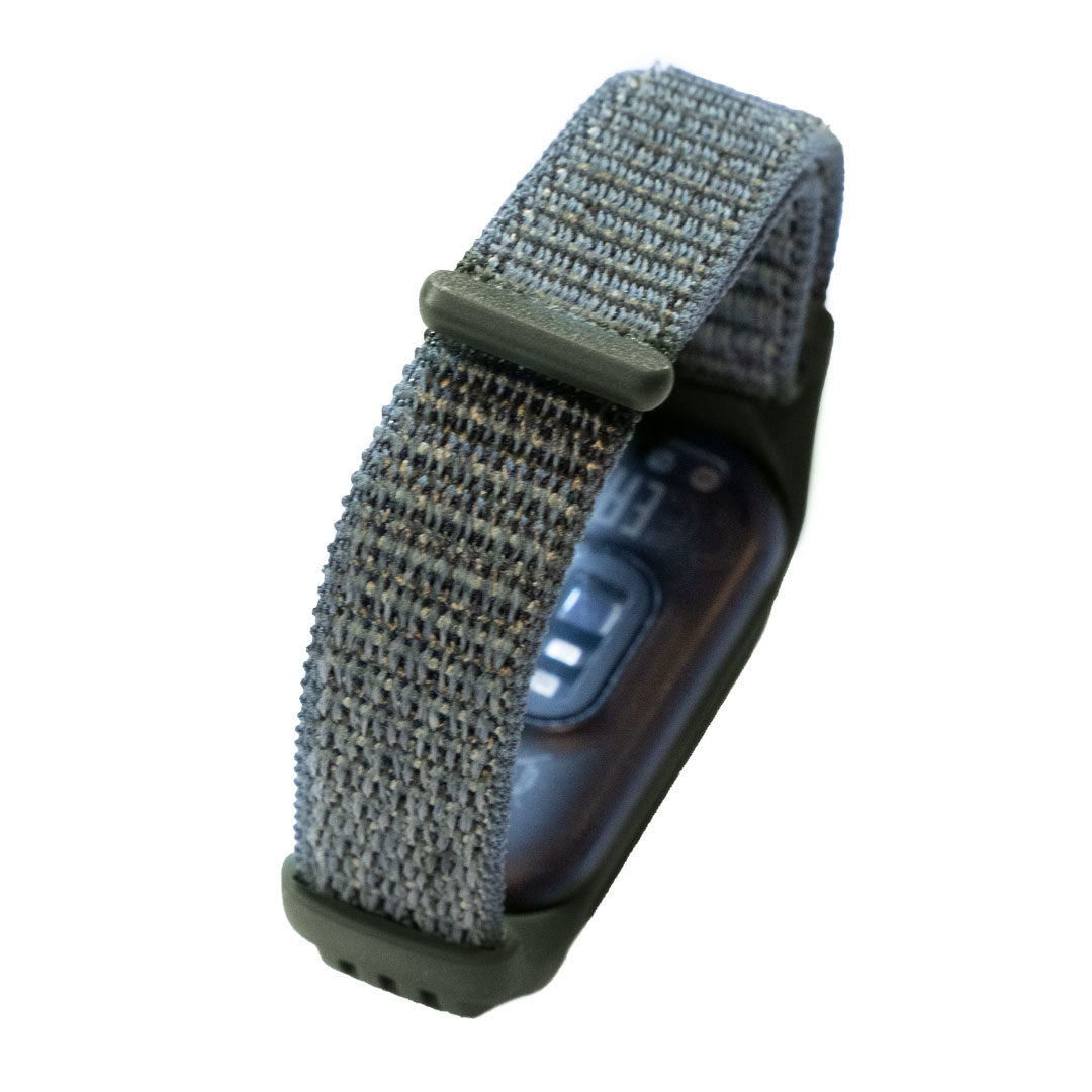 Ein graues und grünes Smartwatch-Armband. Das Armband besteht aus gewebtem Stoff und ist mit einem dunkel gefärbten Zifferblatt verbunden.