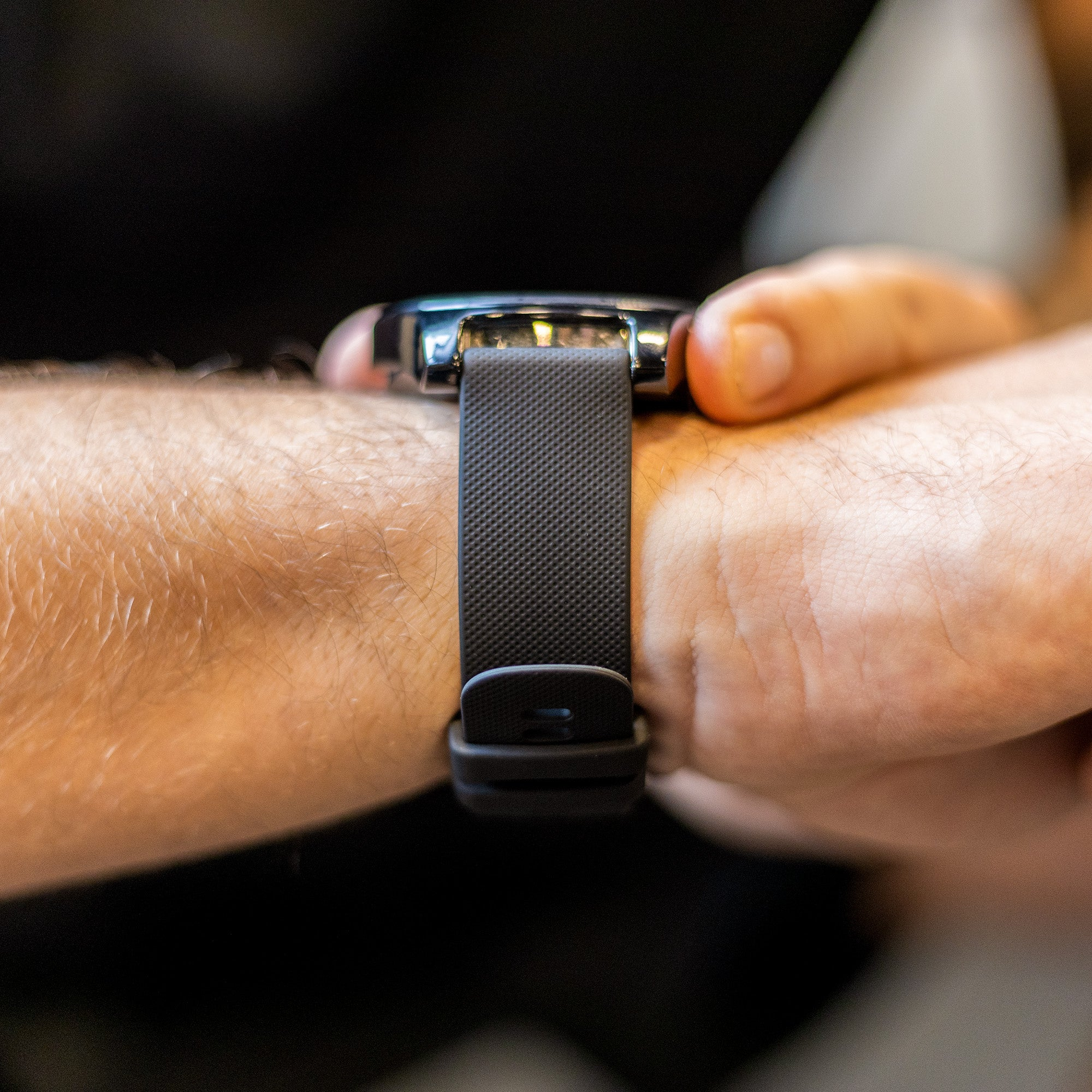Nahaufnahme eines Handgelenks mit einer schwarzen Smartwatch mit strukturiertem Armband, Haut sichtbar.