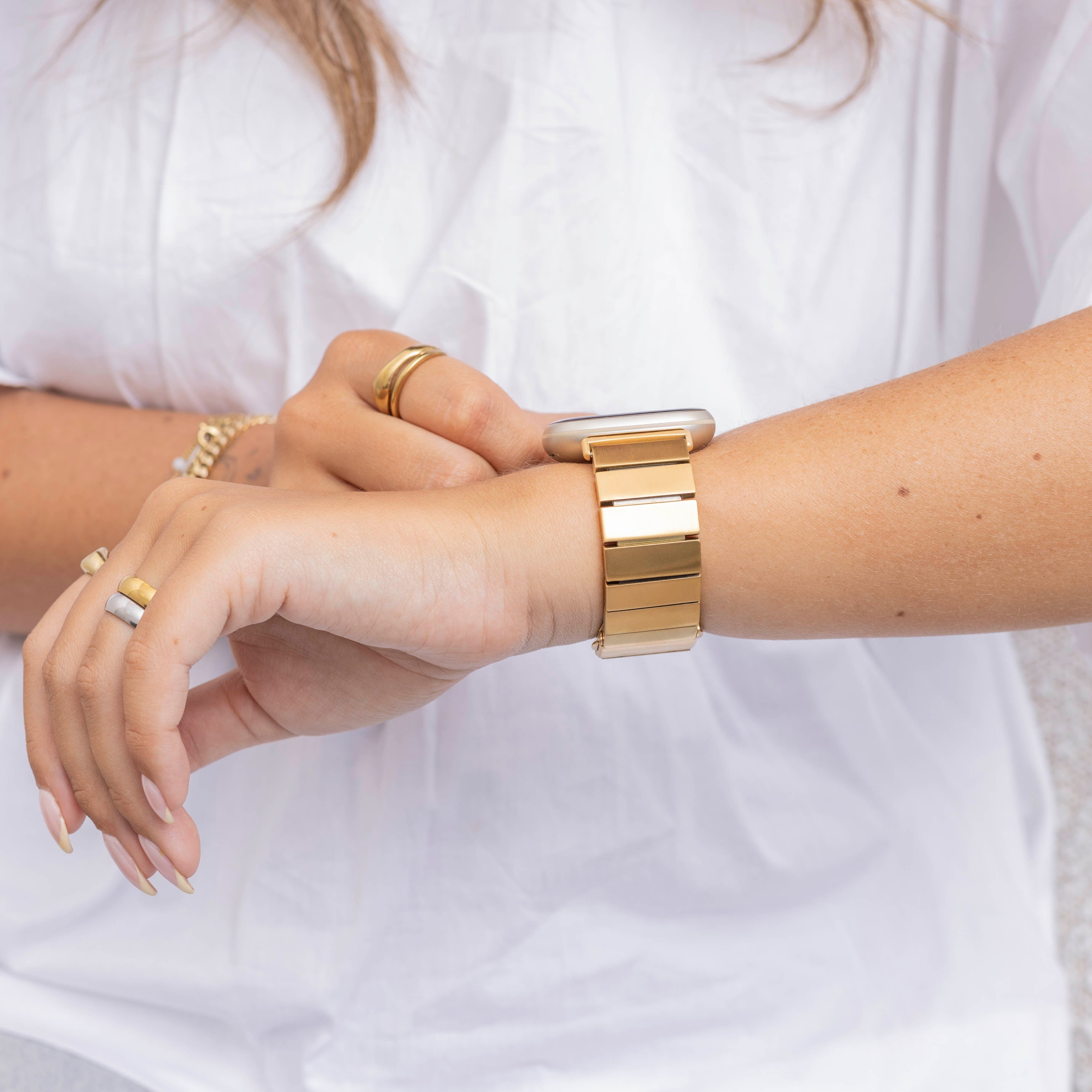 Eine Person mit einer goldenen Uhr und Ringen. Die Person trägt ein weißes Hemd. Die Uhr befindet sich am Handgelenk.