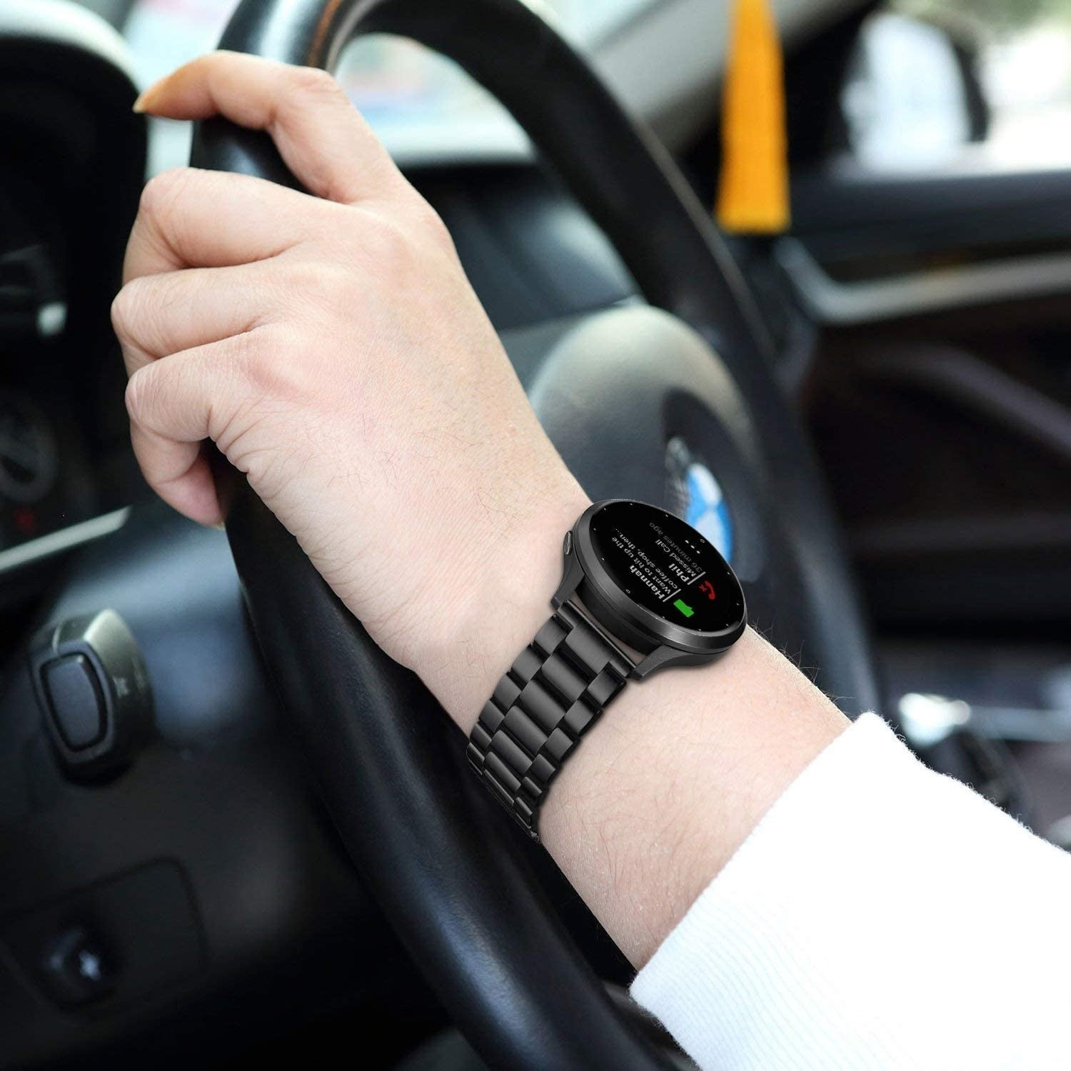Eine Person fährt Auto und trägt eine schwarze Smartwatch am Handgelenk. Die Uhr zeigt einen verpassten Anruf von Hannah an.