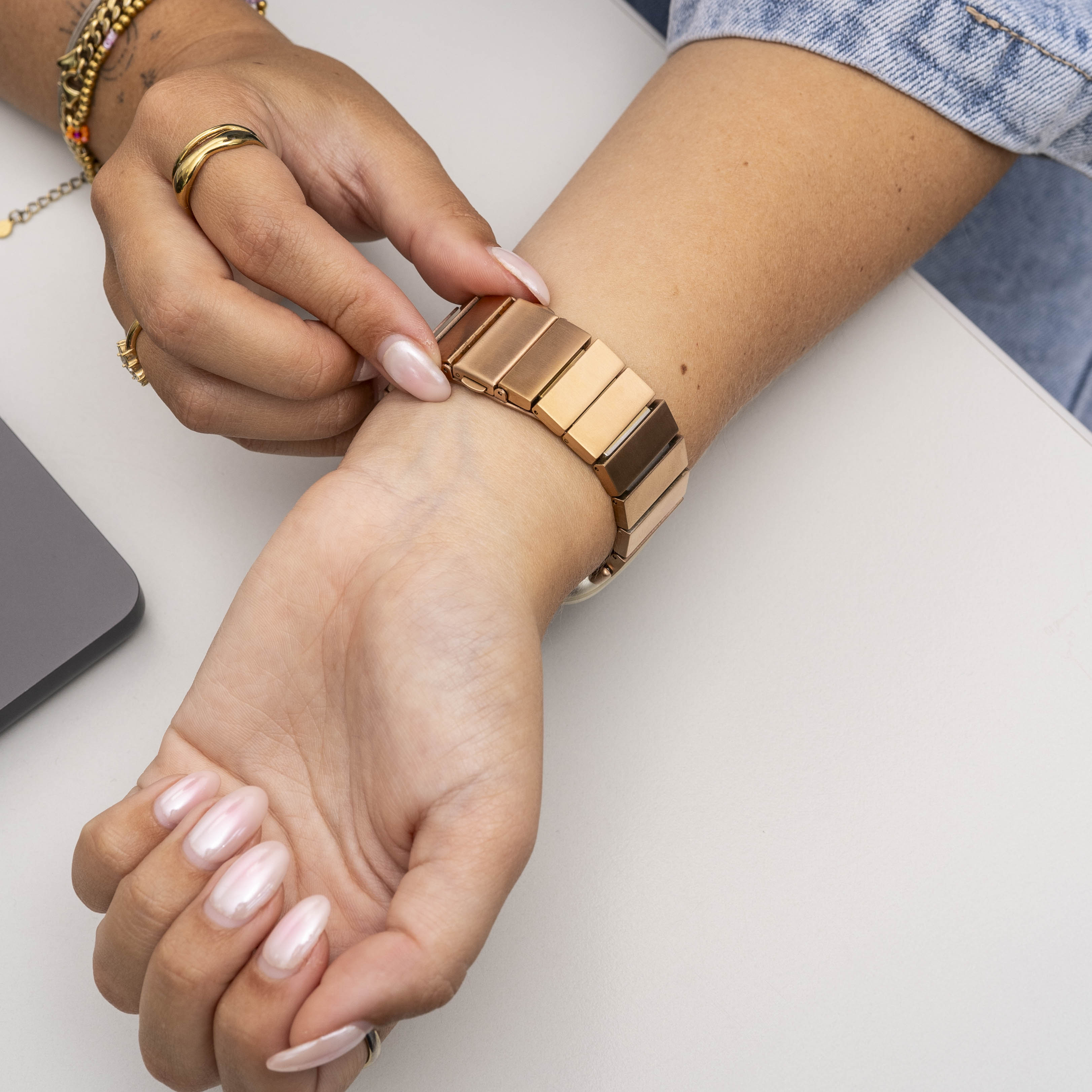 Das Handgelenk einer Person mit einem roségoldenen Armband. Die Hand der Person berührt das Armband. Die Nägel sind rosa lackiert.
