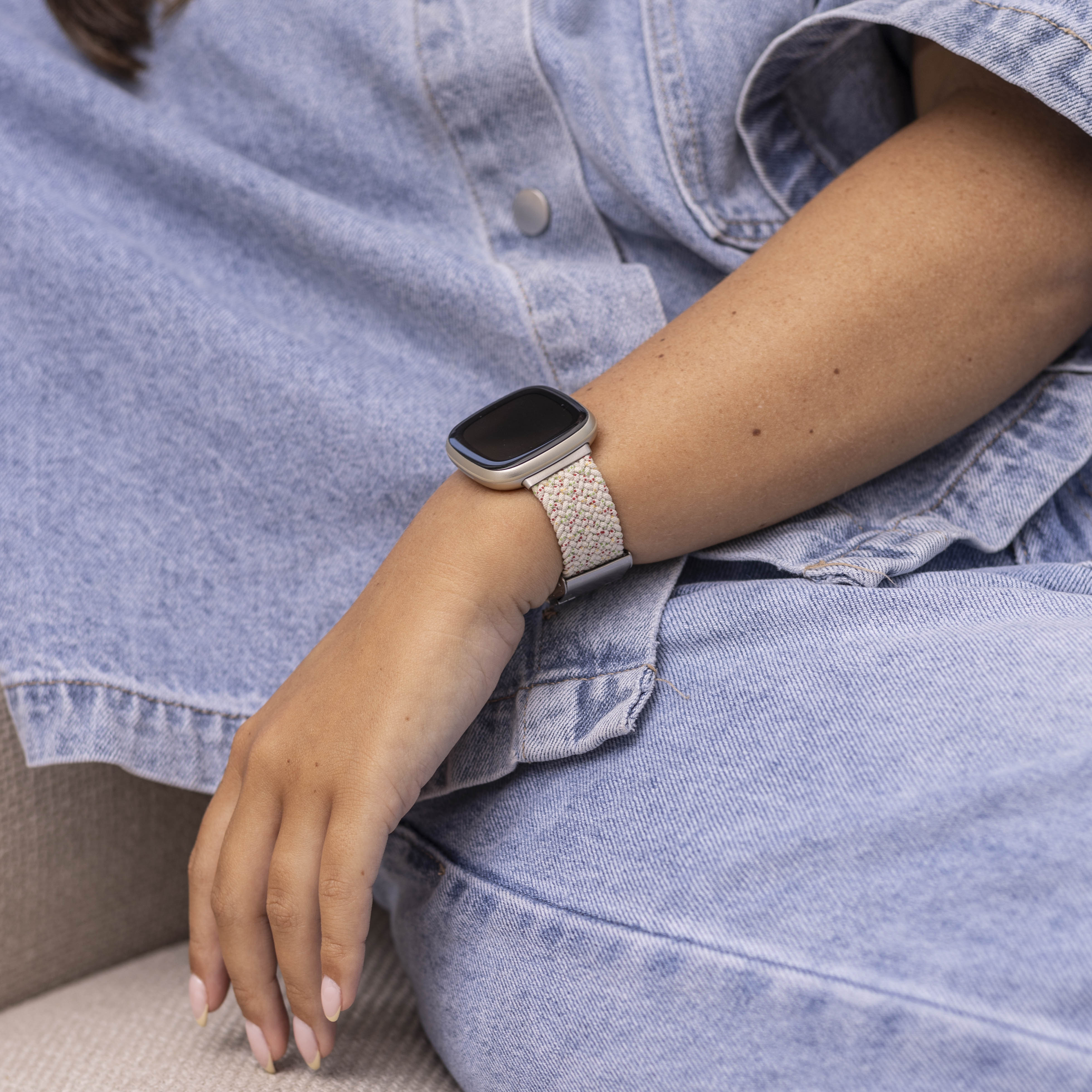 Nahaufnahme eines Arms mit Smartwatch und gemustertem Armband auf Denim-Schoß.