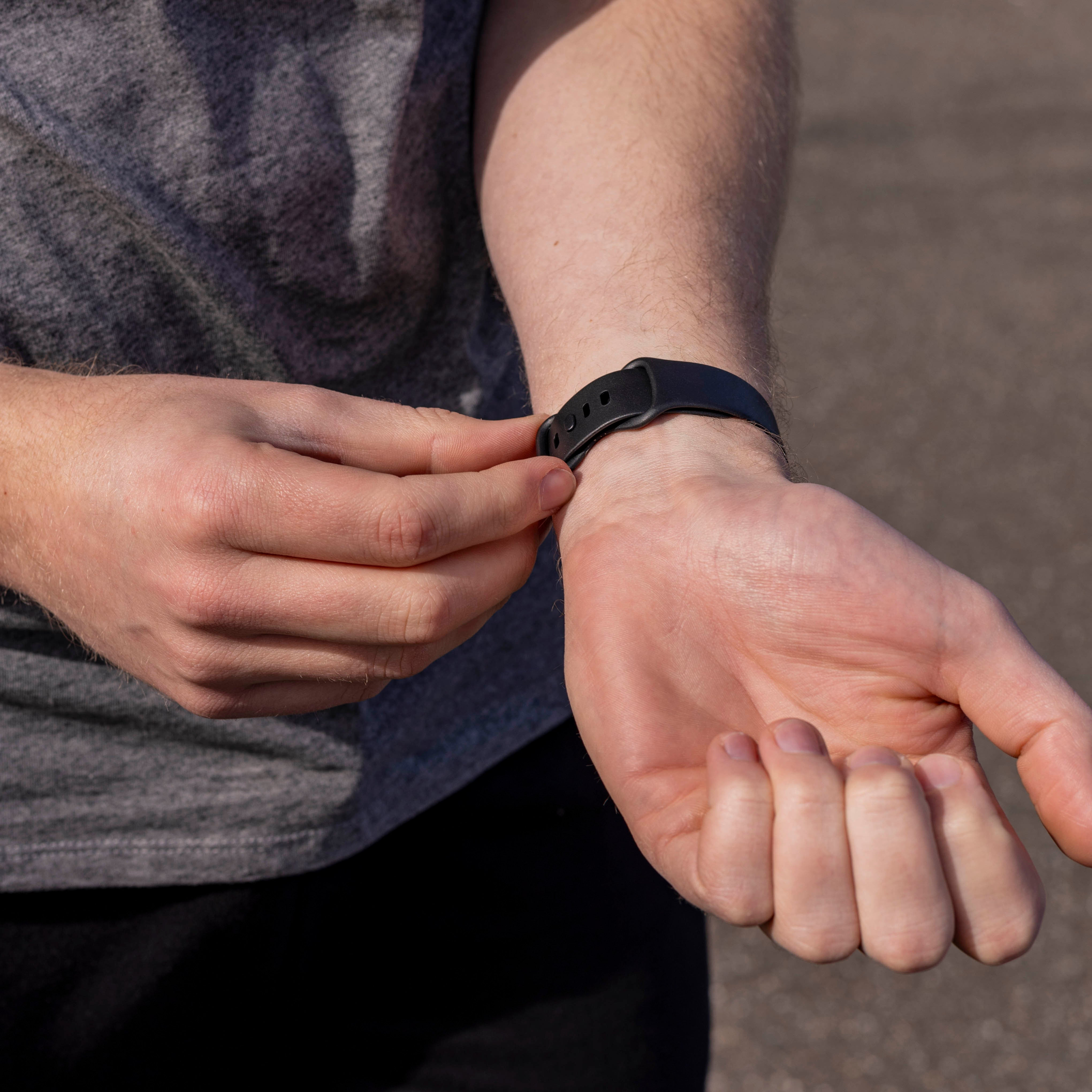 Eine Person stellt eine schwarze Uhr an ihrem Handgelenk ein. Die Szene spielt sich im Freien ab.