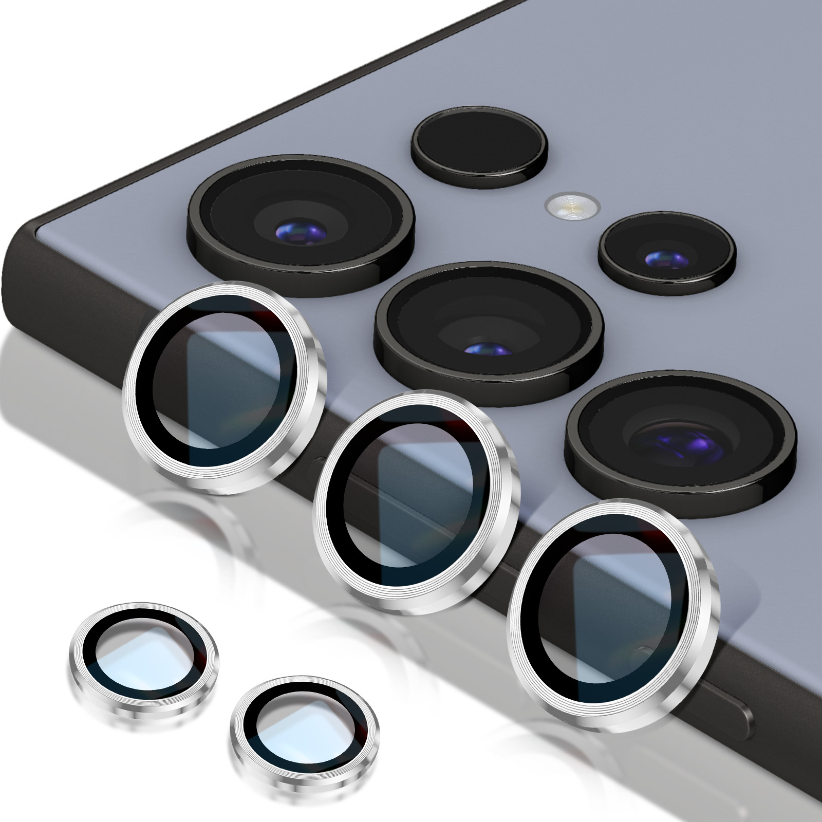 Un teléfono inteligente con múltiples lentes de cámara. También hay varios protectores de lentes plateados, algunos colocados en el teléfono, otros sueltos.