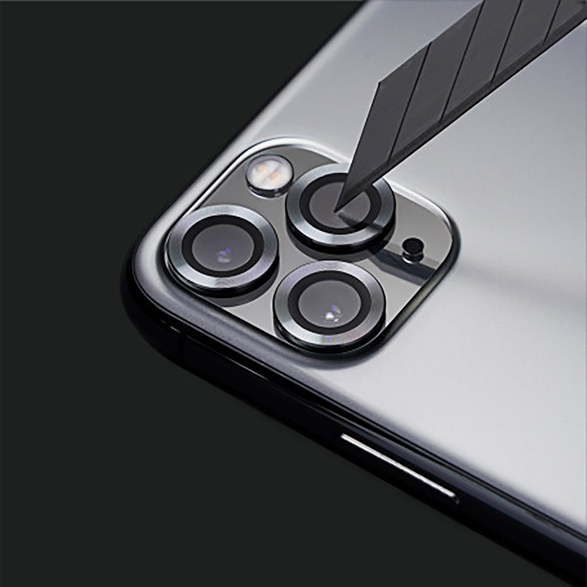 Close-up van een telefoon cameramodule met een mes. De module heeft vier lenzen en een flitser. Het mes snijdt de lens.
