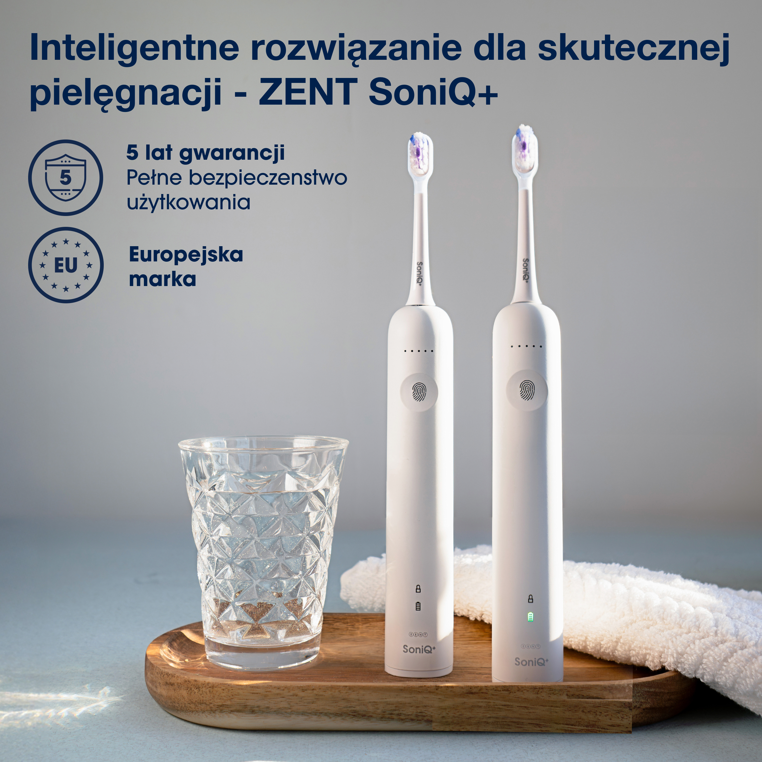 Dwie białe elektryczne szczoteczki do zębów, szklanka wody i ręcznik na drewnianej tacy. U góry tekst w języku polskim.