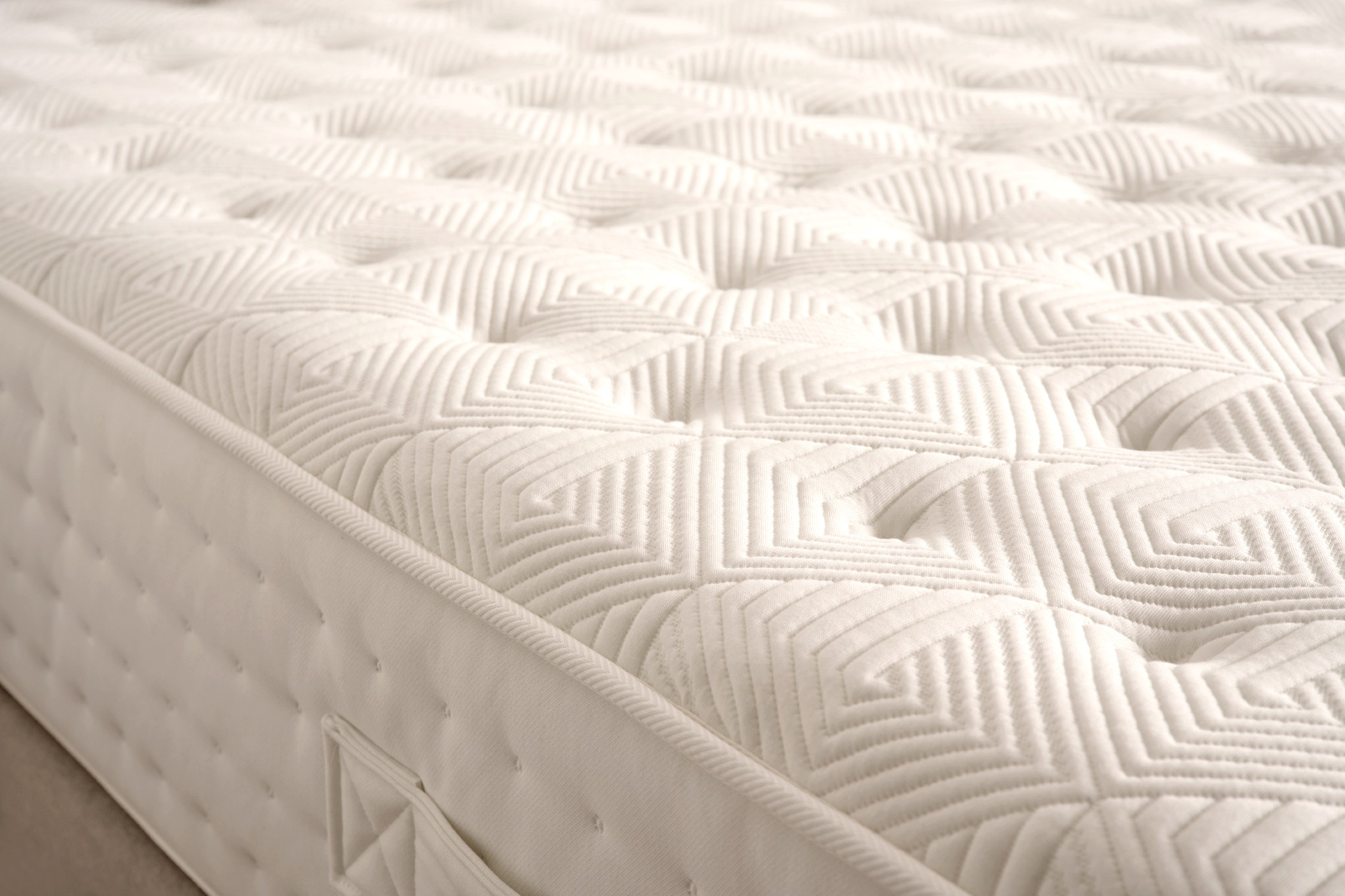 Primer plano de un colchón blanco con patrones geométricos y laterales cosidos. Parece suave y acogedor, con una superficie texturizada.