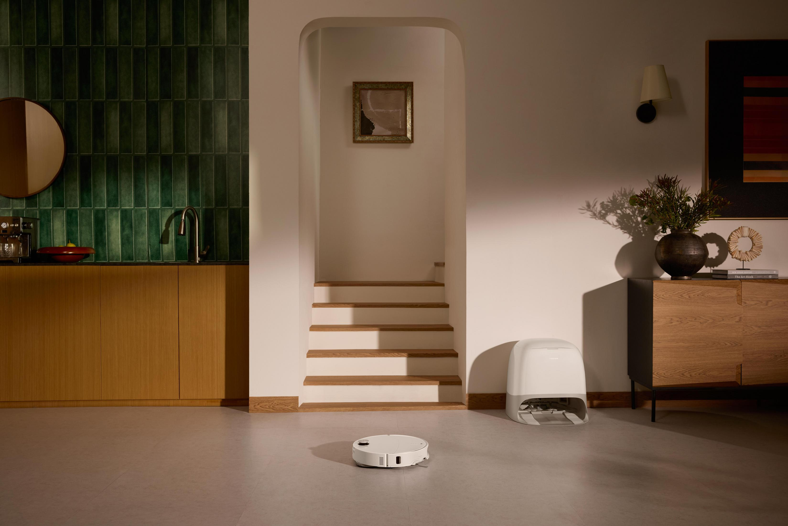 Nowoczesne wnętrze z odkurzaczem, schodami i zielonymi kafelkami. Widoczna szafka, sztuka i odkurzacz robot.