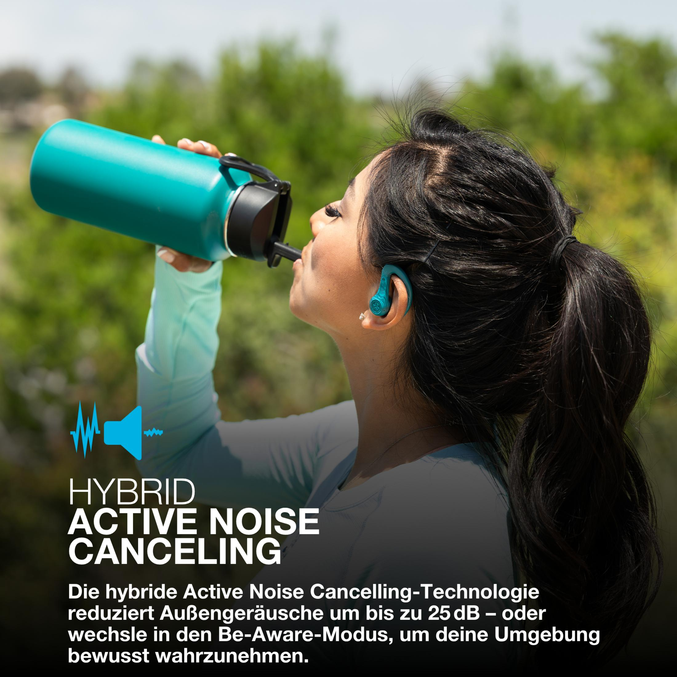 Kobieta pije z turkusowej butelki z wodą, nosząc turkusowe słuchawki. Tło to zielony, rozmyty park.