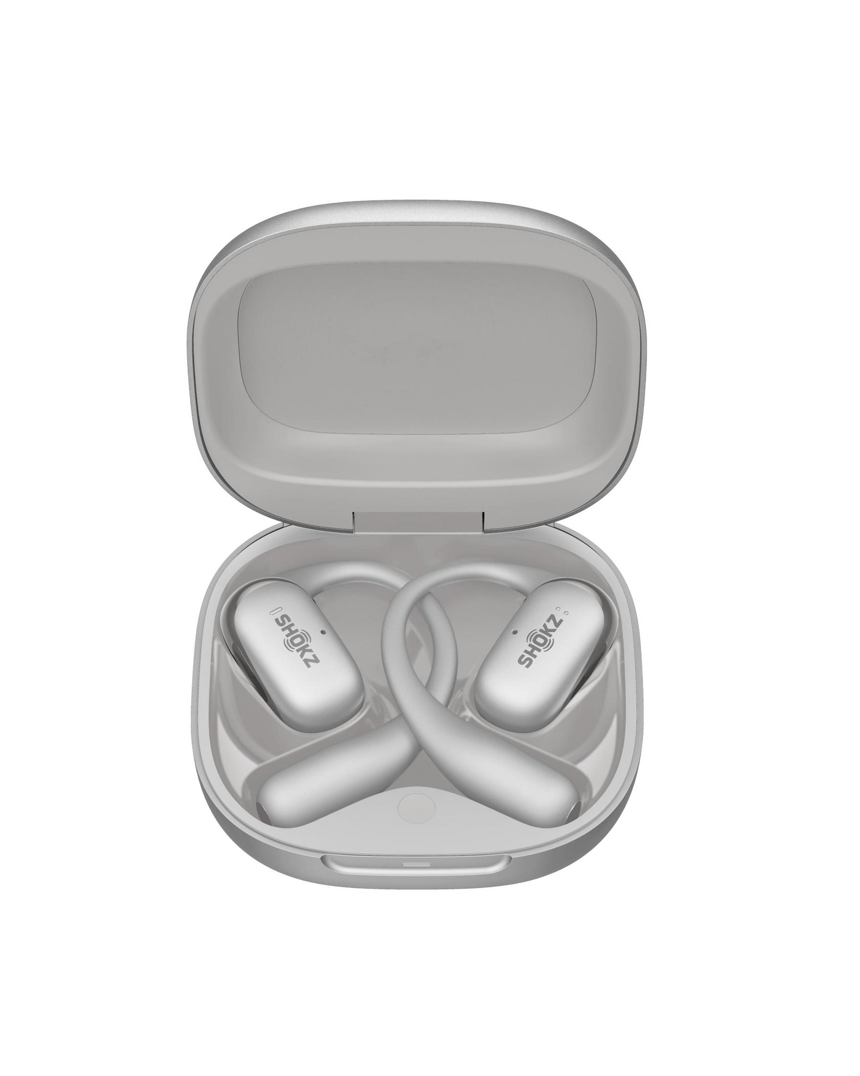 Otwarte etui ze srebrnymi słuchawkami. Etui jest otwarte, pokazując kształt słuchawek. Słuchawki mają napis SHOKZ. Białe tło.