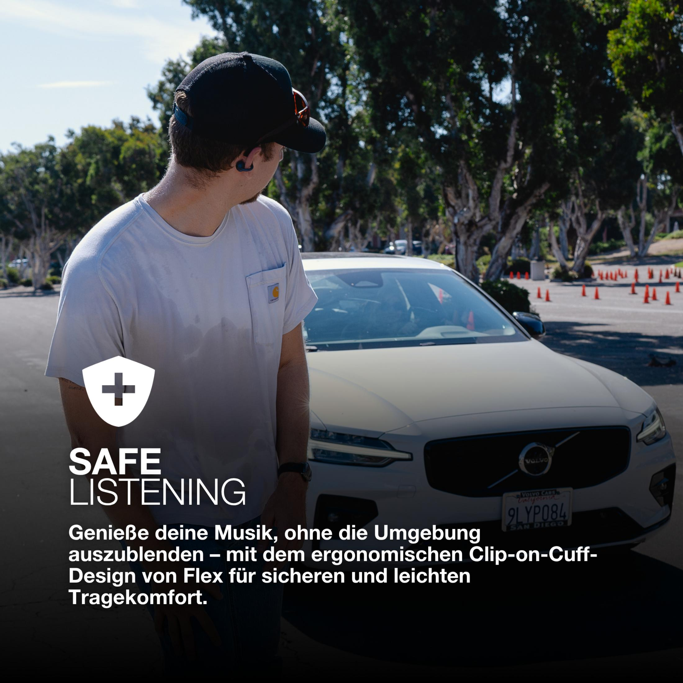 Un homme en chemise blanche et casquette noire regarde ailleurs. Une voiture blanche en arrière-plan. Superposition de texte : Écoute sûre.