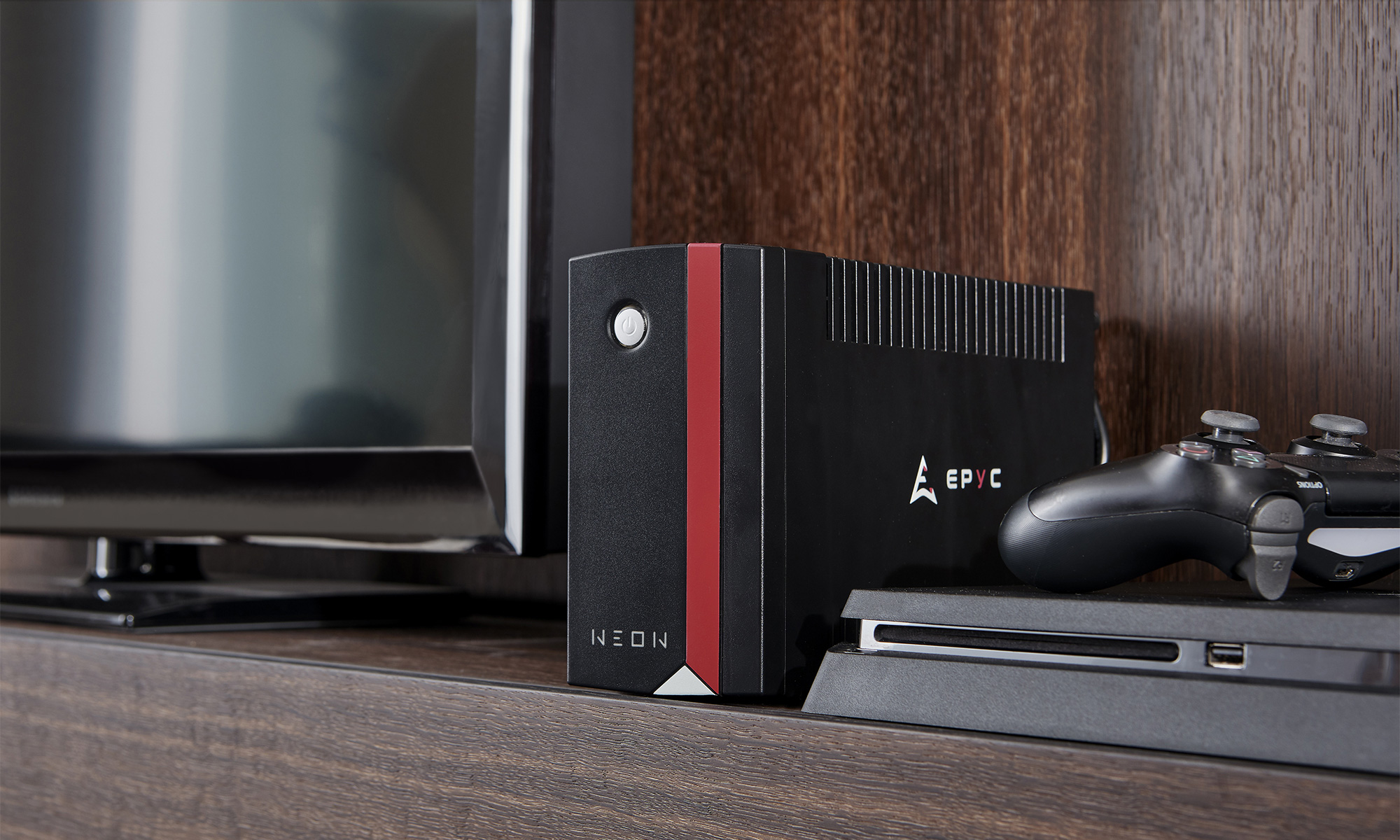 Una console di gioco nera con una striscia rossa, un controller e una TV su una mensola di legno. La console ha la scritta 'NEON'.