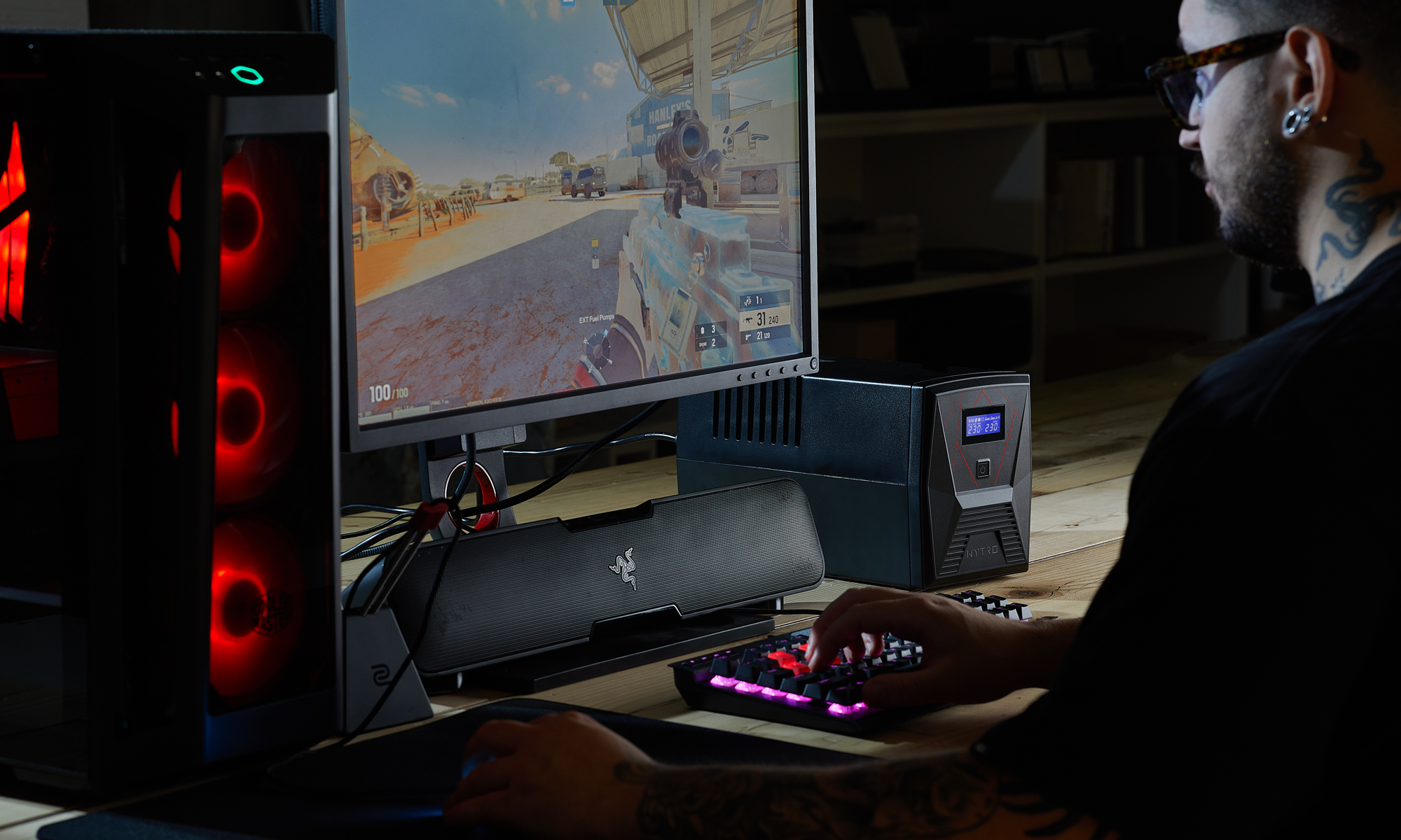 Un uomo sta giocando al computer. Lo schermo mostra un gioco sparatutto in prima persona. Un PC da gioco illuminato di rosso è a sinistra.