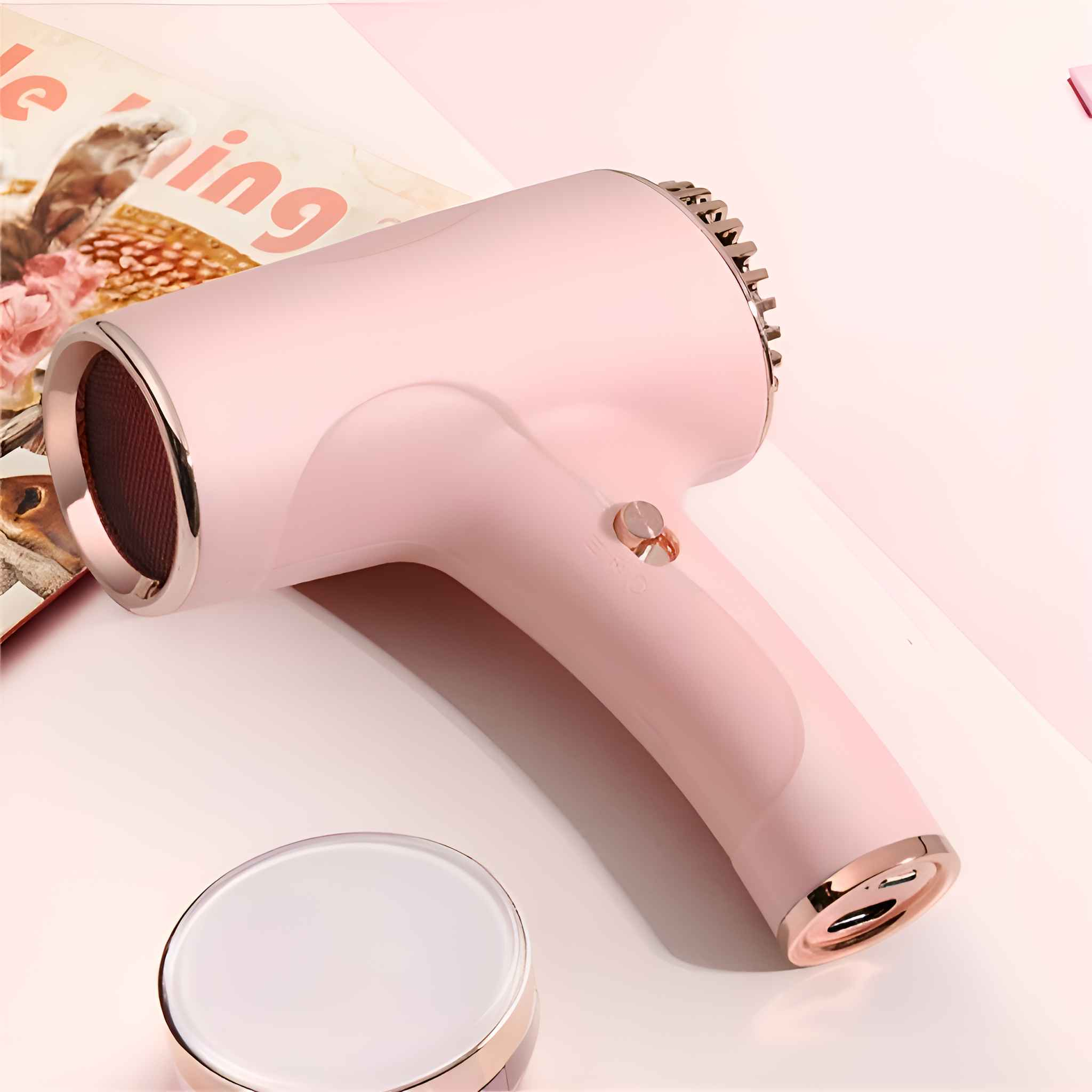 Ein rosa Haartrockner mit goldenen Akzenten liegt auf einer rosa Oberfläche, neben einem kleinen Behälter und einer Zeitschrift.