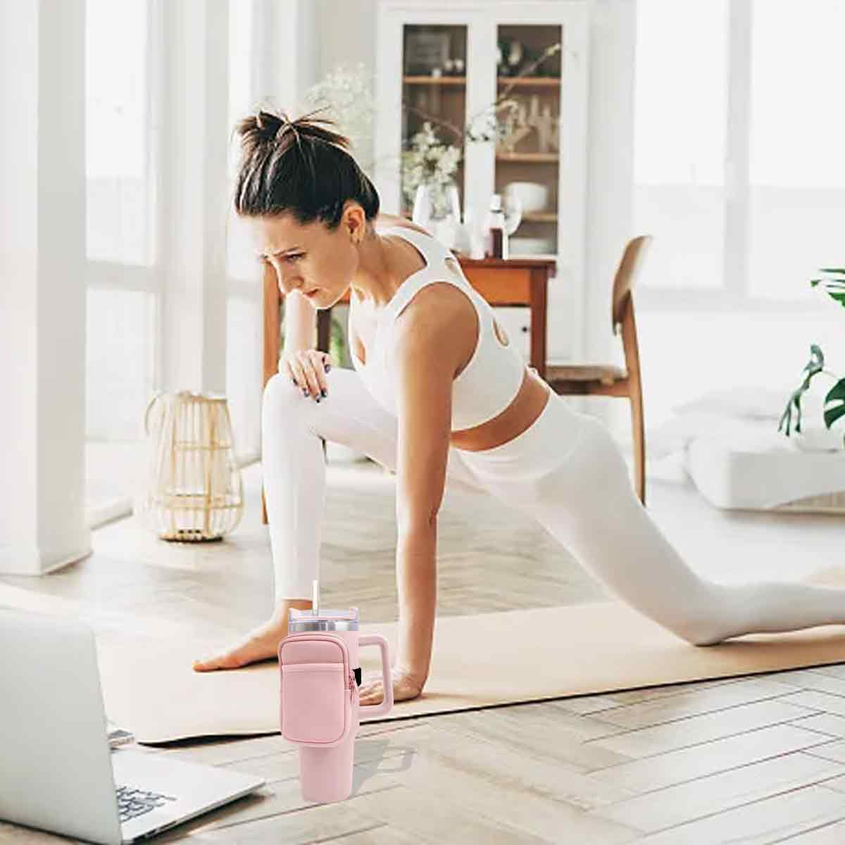 Frau in weißer Sportkleidung dehnt sich auf einer Matte. Eine rosa Wasserflasche mit Griff steht im Vordergrund. Ein Laptop ist links.