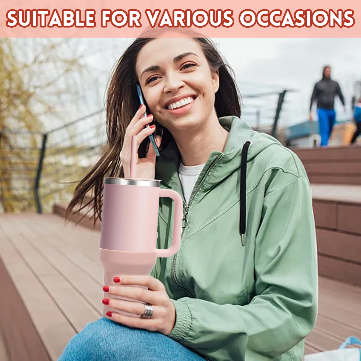 Eine lächelnde Frau hält einen rosa Becher mit Strohhalm und telefoniert. Sie trägt eine grüne Jacke und sitzt draußen.
