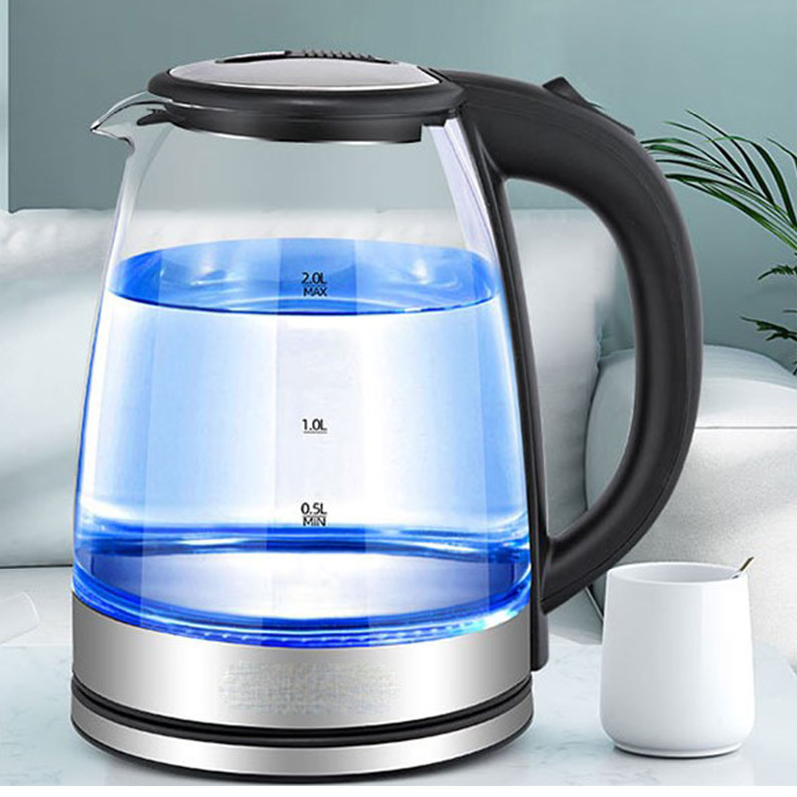 Ein elektrischer Glaskessel mit blauem Wasser, einem schwarzen Griff und einer weißen Tasse mit einem Löffel auf einem Tisch.