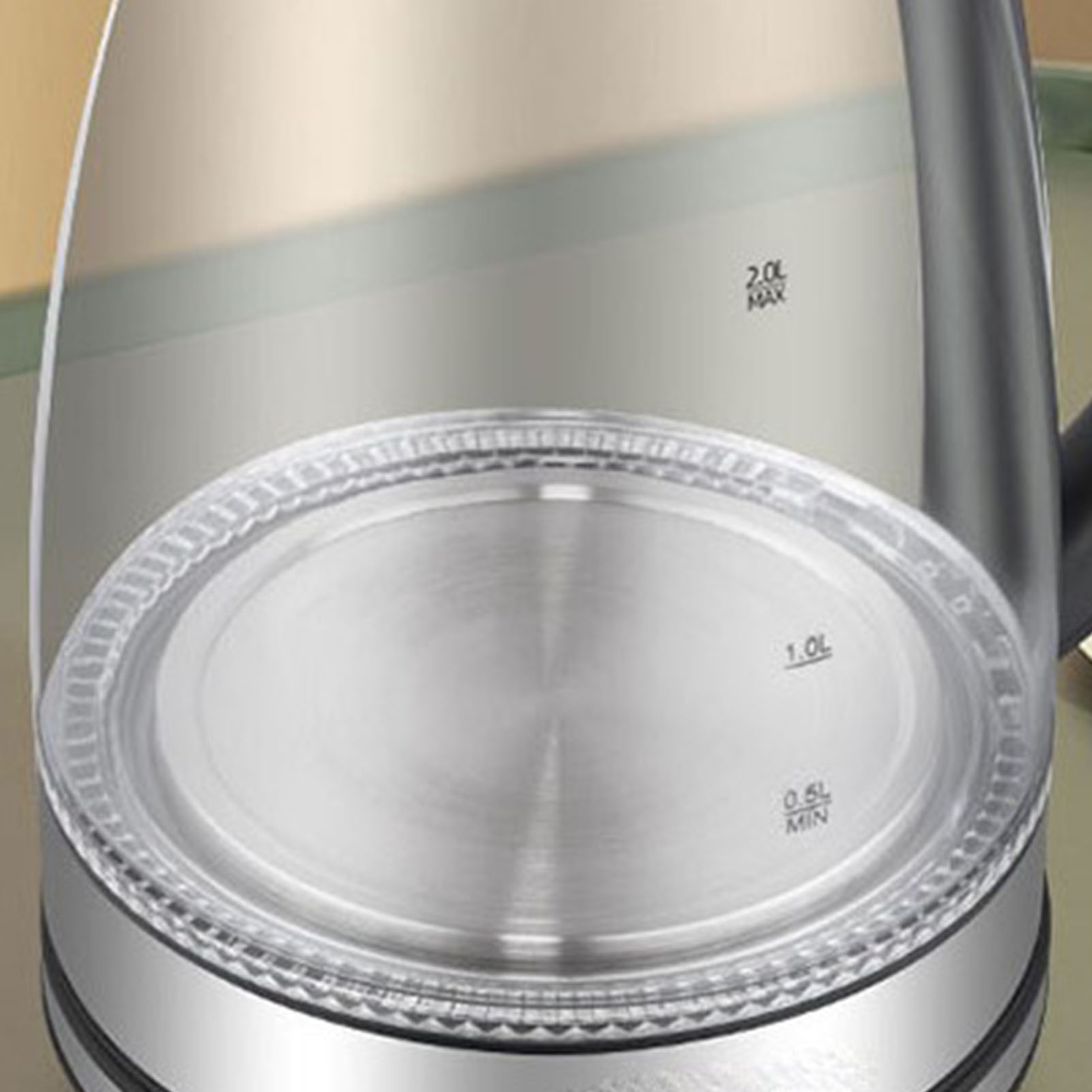 Nahaufnahme eines transparenten Wasserkochers mit Edelstahlboden und Deckel. Kapazitätsmarkierungen sind sichtbar. Der Hintergrund ist unscharf.
