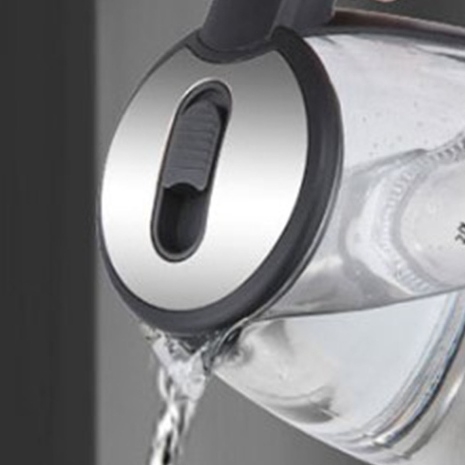 Ein Wasserkocher gießt Wasser aus. Der Wasserkocher ist silber und schwarz, das Wasser klar. Der Hintergrund ist grau.