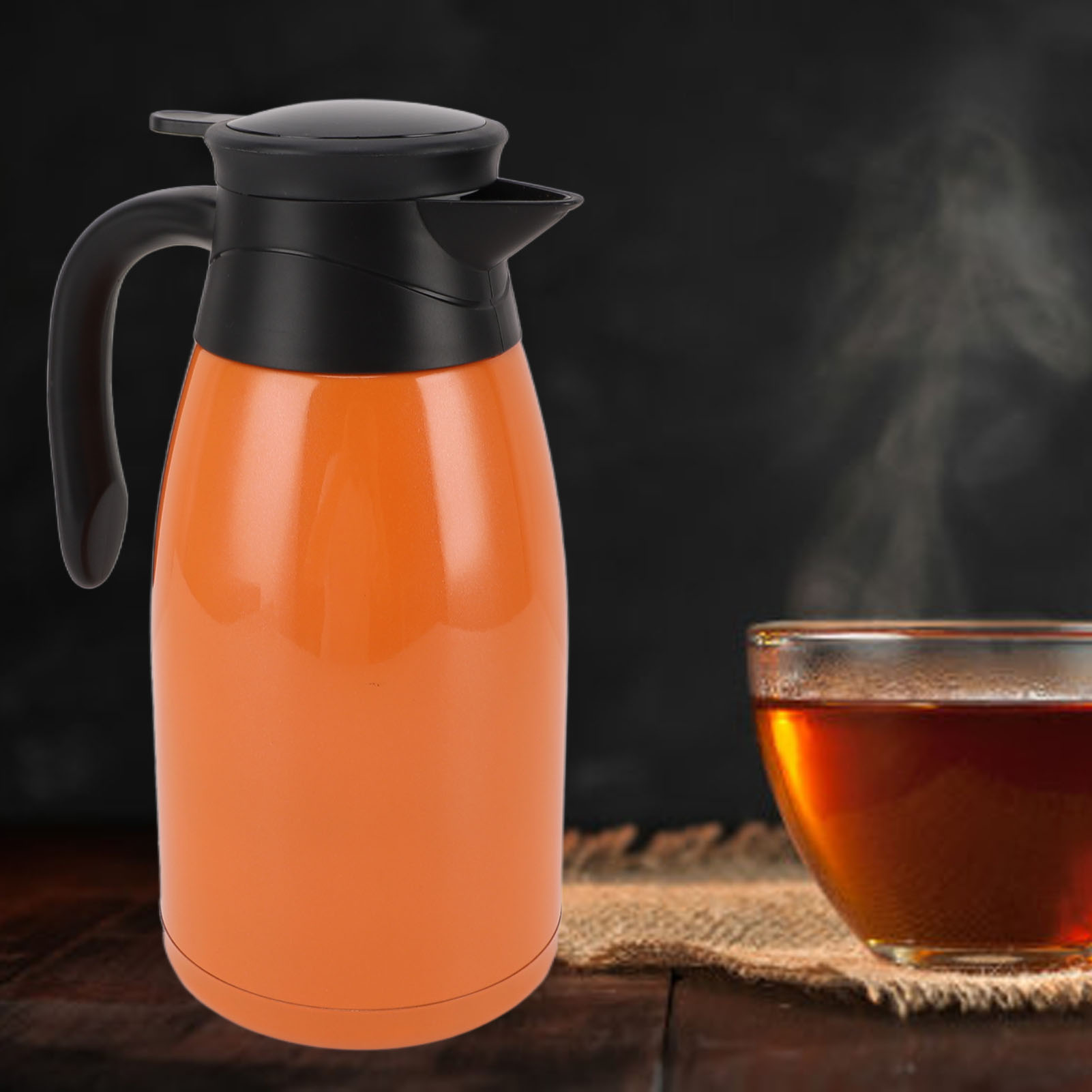 Orangene Thermoskanne mit schwarzem Deckel und Griff, neben einer Tasse Tee. Dampf steigt vom Tee auf. Dunkler Hintergrund.