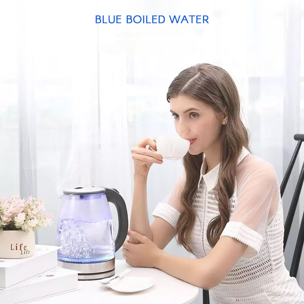 Eine Frau trinkt aus einer Tasse in der Nähe eines kochenden Wasserkochers. Auf dem Tisch stehen ein Blumentopf und ein Teller. Das Wasser ist blau.