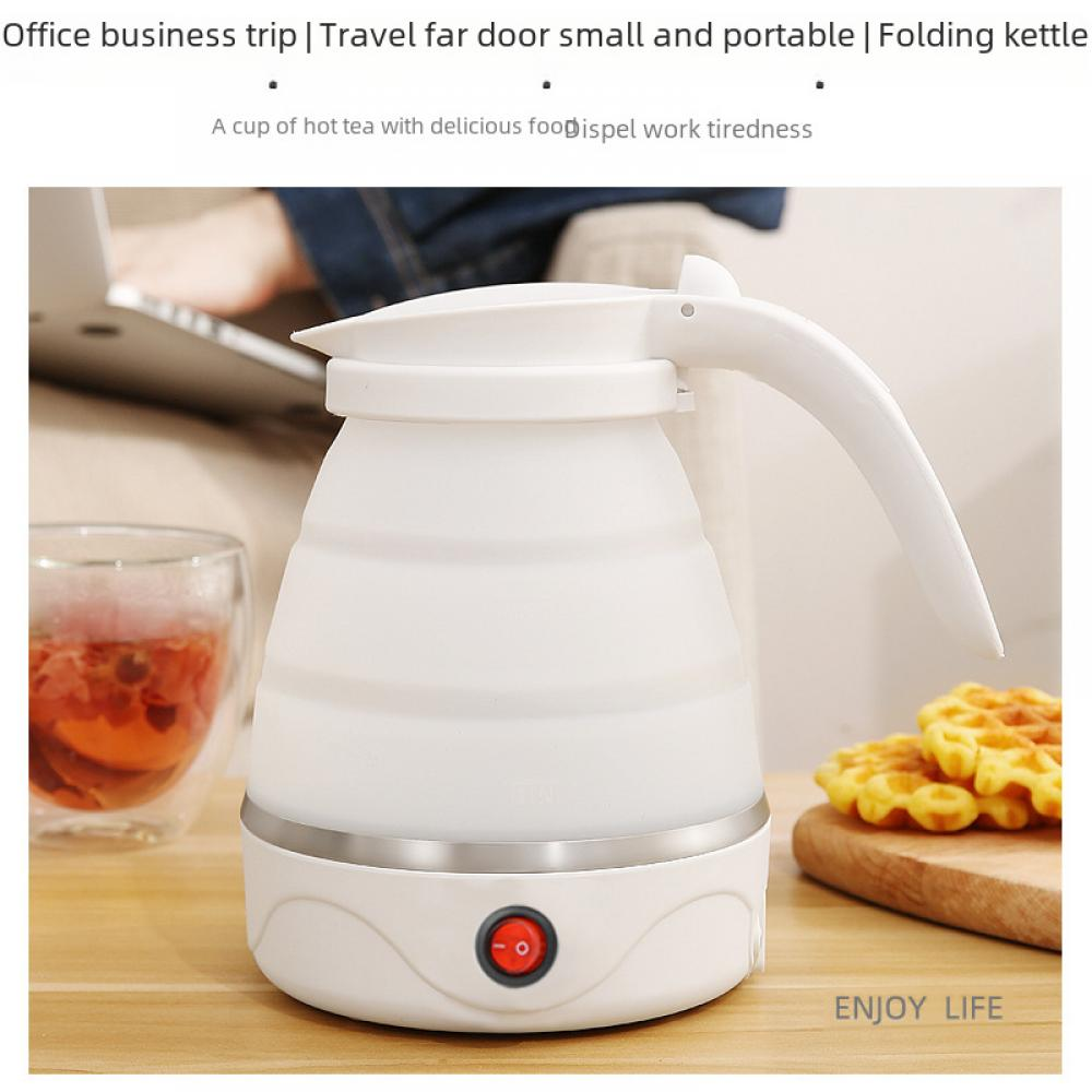 Ein weißer Faltkocher steht auf einem Tisch neben einem Glas Tee und Waffeln. Im Hintergrund ist eine Person, die einen Laptop benutzt.
