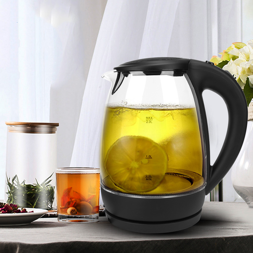 Ein Glaskessel mit Tee und einer Zitronenscheibe. Ein Glas Tee, Gläser und Blumen stehen auf dem Tisch.