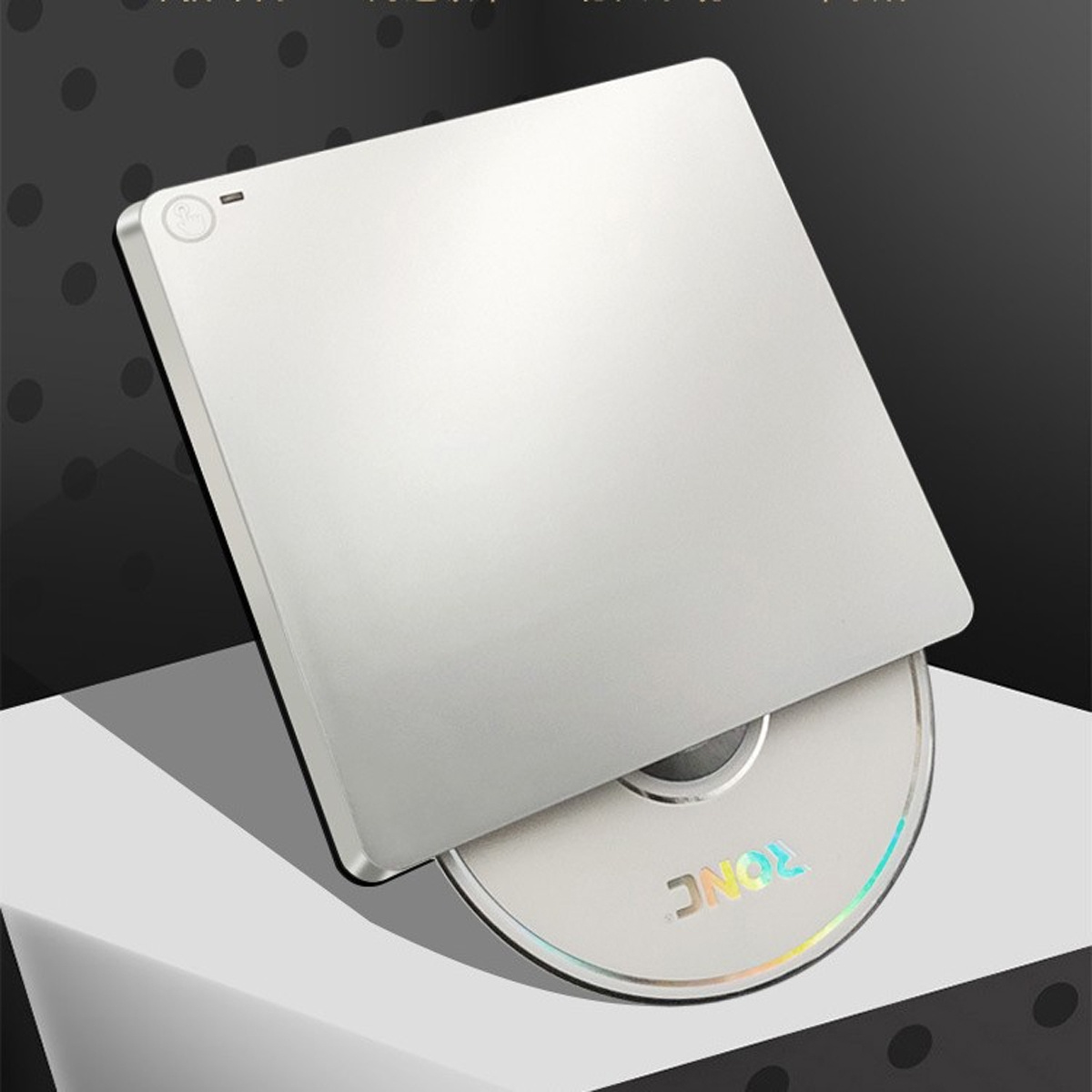 Ein silbernes externes CD/DVD-Laufwerk mit teilweise eingelegter Disc. Es liegt auf einer weißen Oberfläche mit schwarzem und grauem Hintergrund.