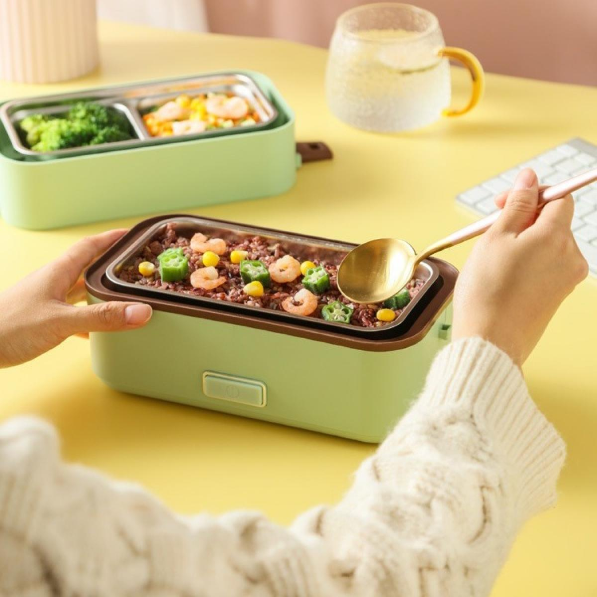 Eine Person hält einen goldenen Löffel über einer grünen Lunchbox mit Essen, einschließlich Garnelen, Okra und Mais. Im Hintergrund steht eine Tasse Wasser.