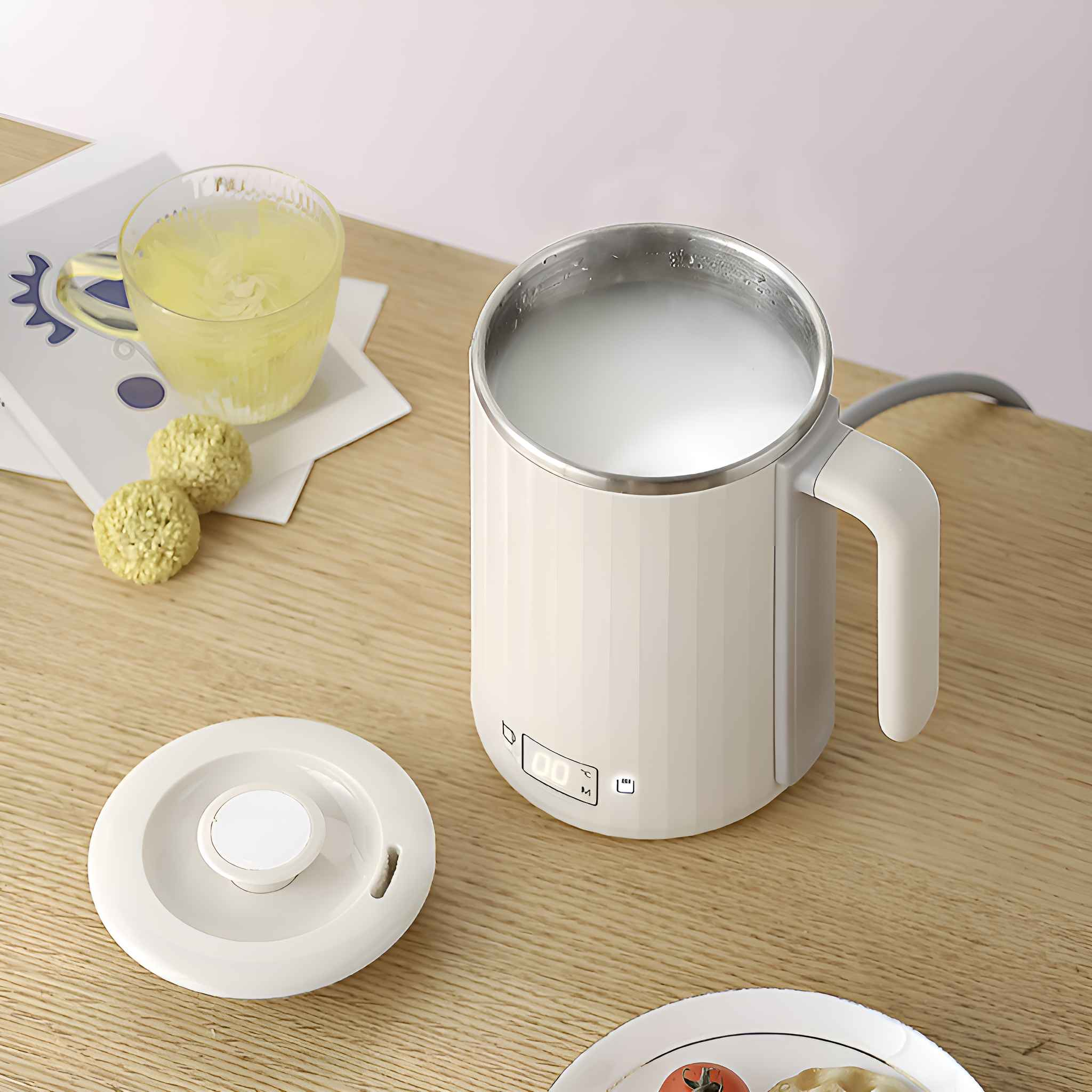 Ein weißer Wasserkocher mit Flüssigkeit, ein Glas mit gelber Flüssigkeit und einige runde Gebäckstücke stehen auf einem Holztisch.