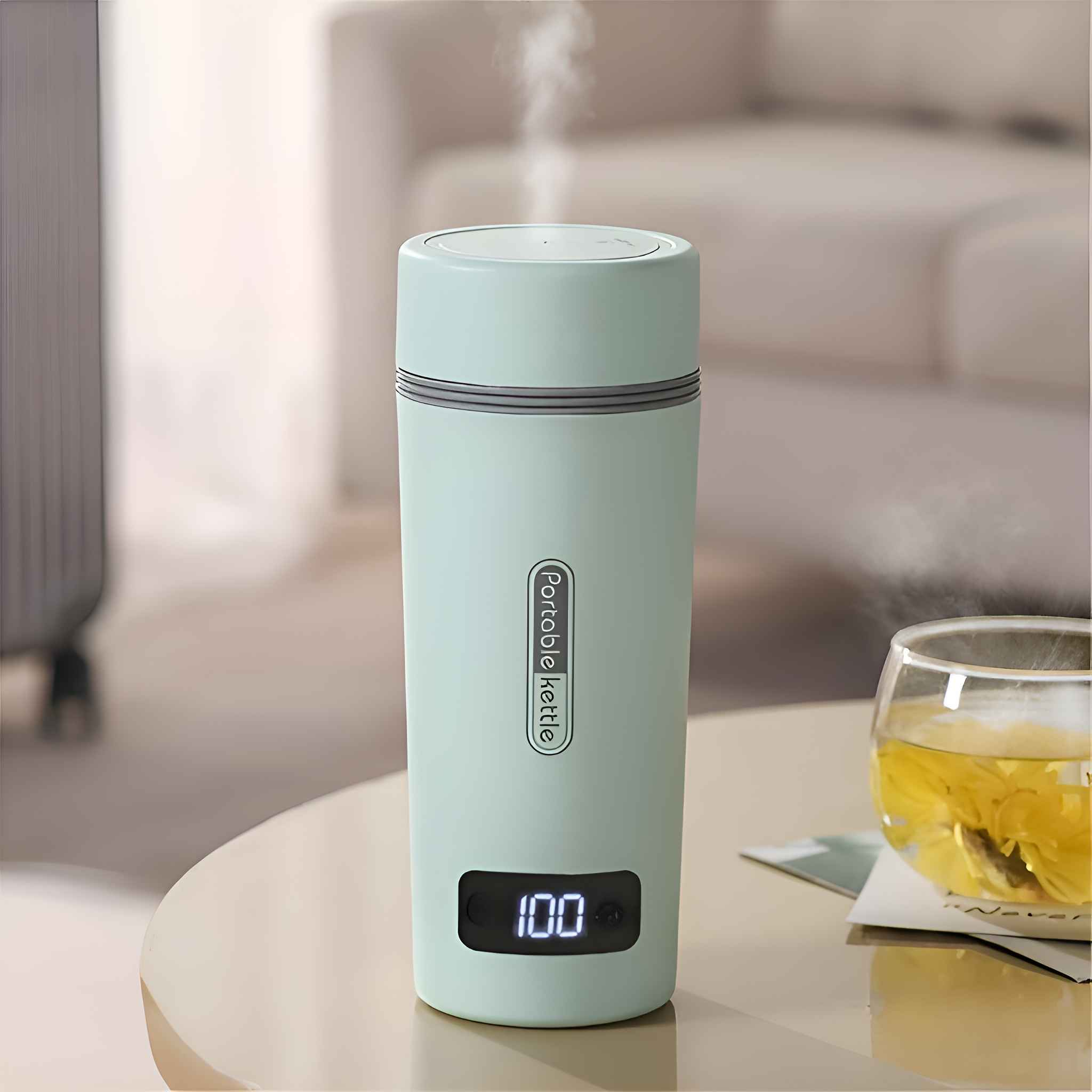 Ein mintgrüner tragbarer Wasserkocher mit Dampf, der '100' anzeigt, steht auf einem Tisch. Ein Glas Tee steht ebenfalls auf dem Tisch.